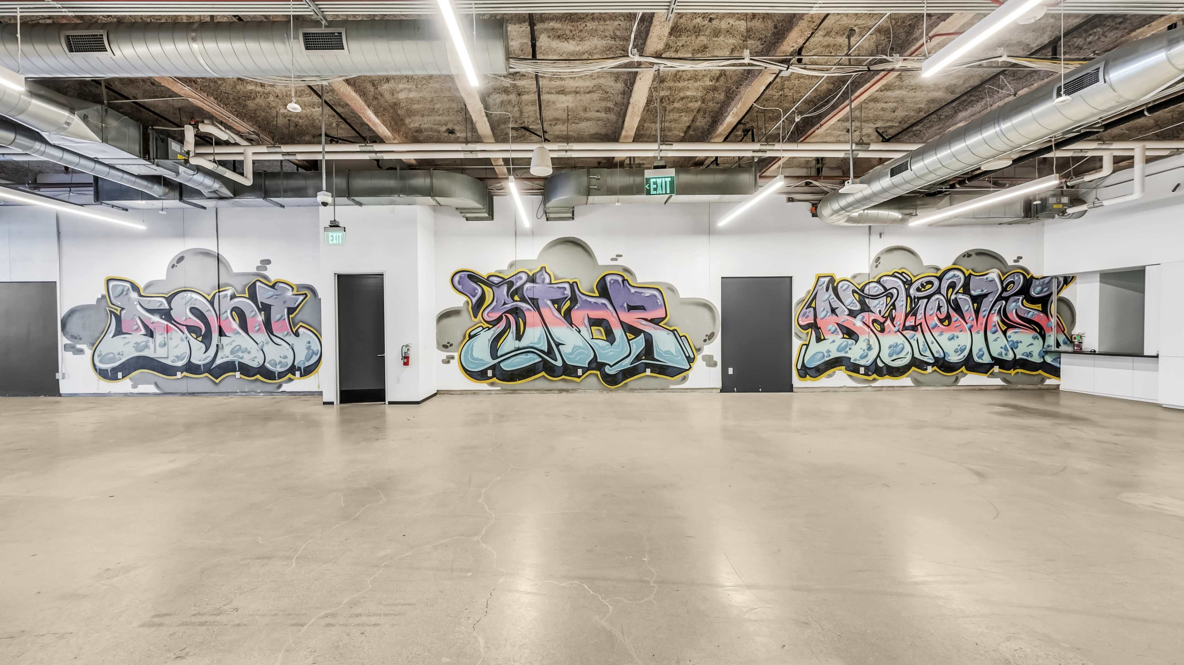 An industrial-style room with concrete flooring and two walls adorned with colorful graffiti.