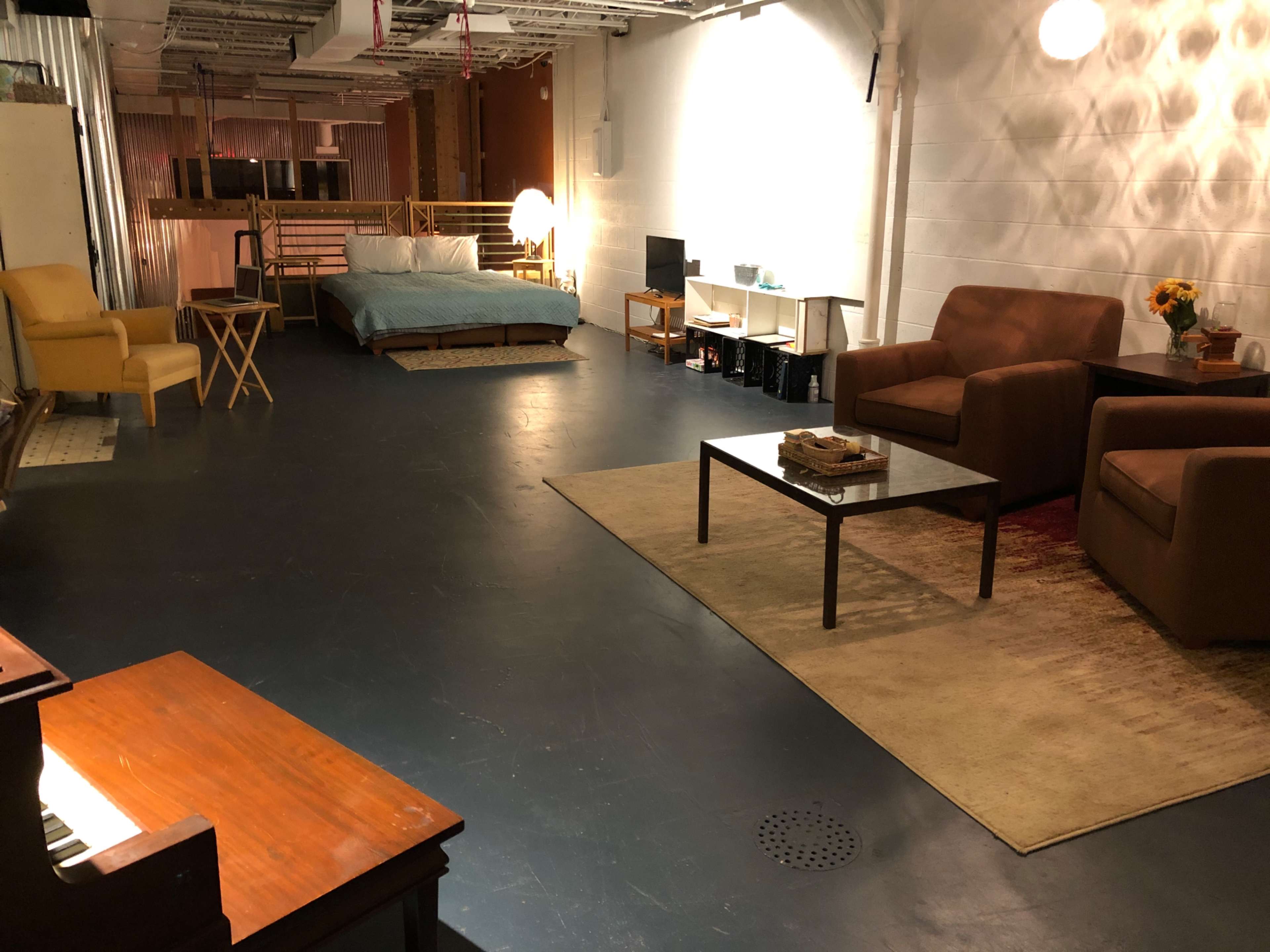 A spacious room with a bed, two seating areas, a small table, and a piano, all arranged on a polished floor.
