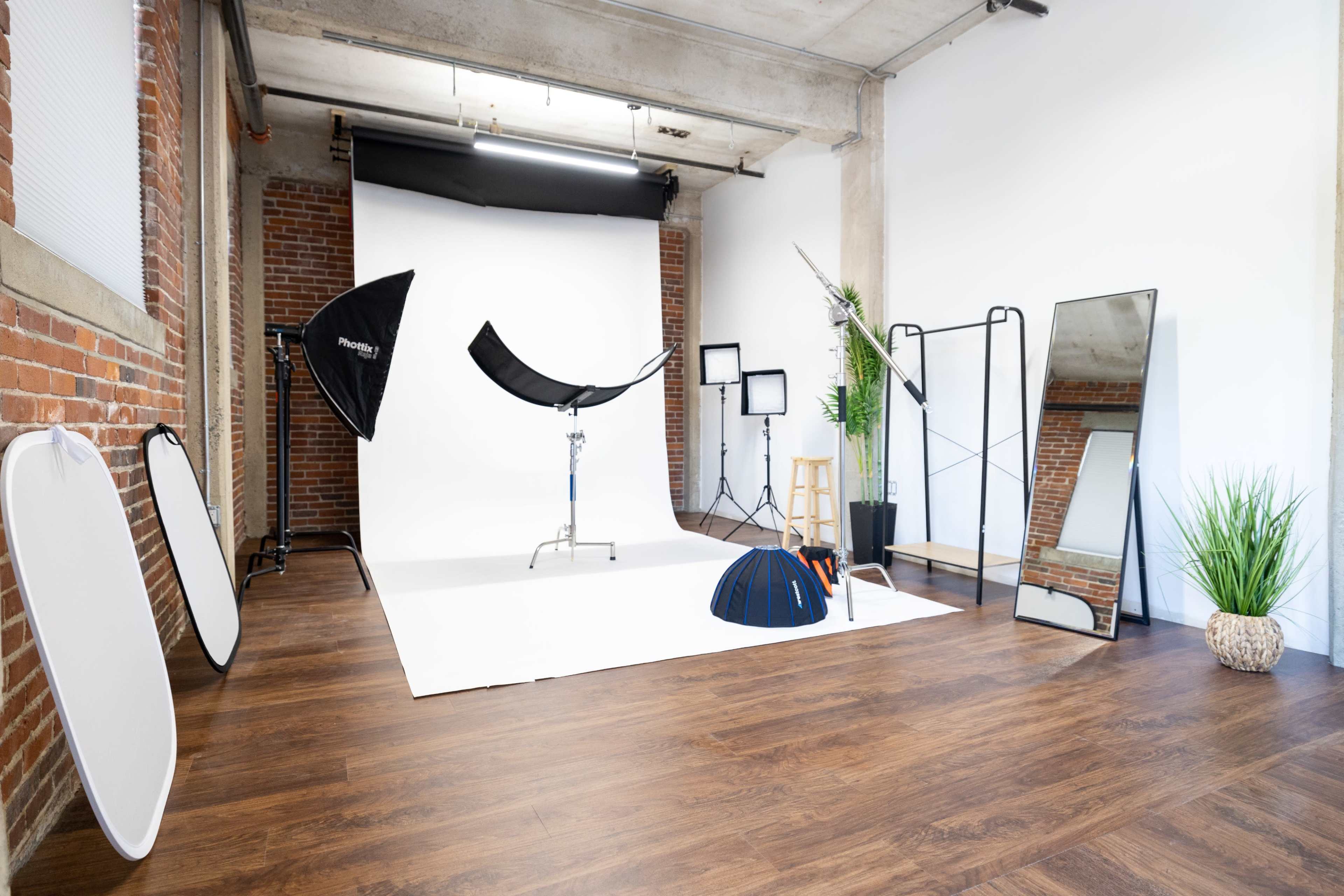 A photography studio setup with various equipment including backdrops, light stands, reflectors, and a mirror.