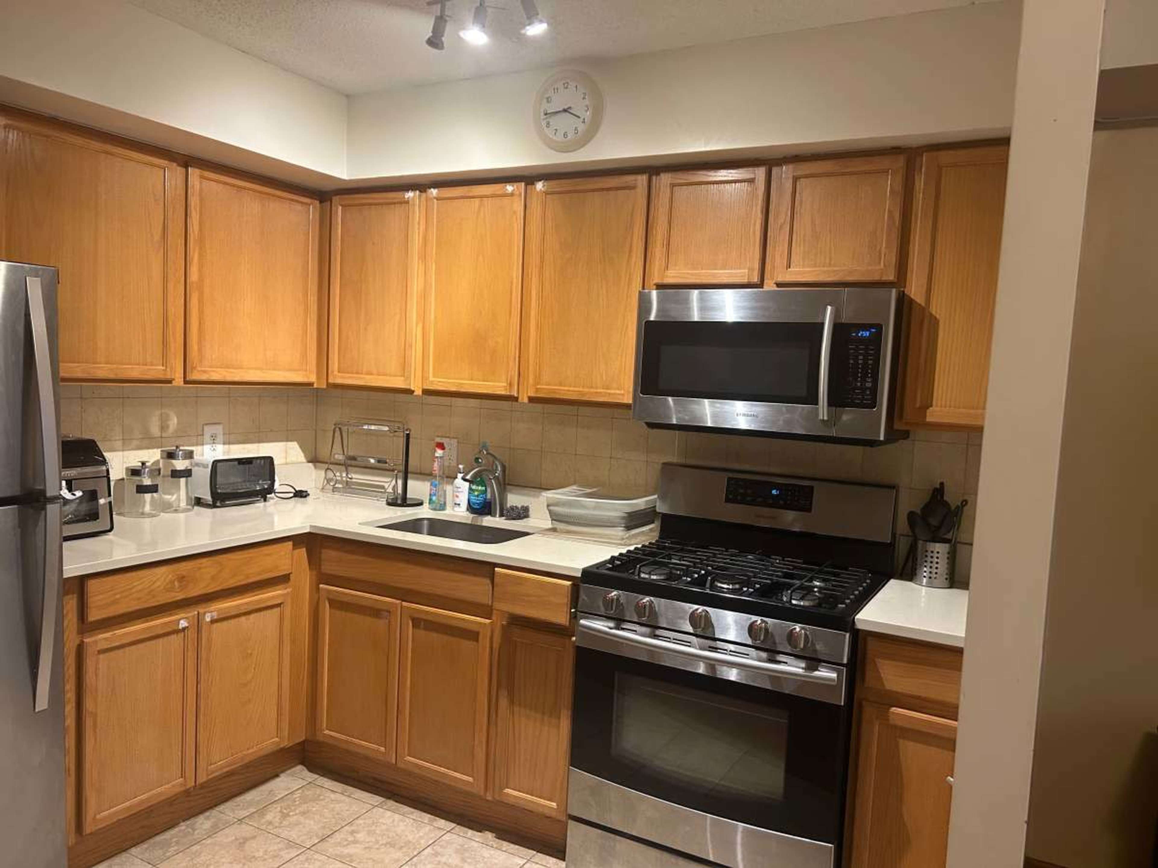 The image shows a modern kitchen featuring wooden cabinets, stainless steel appliances, and a tiled floor.