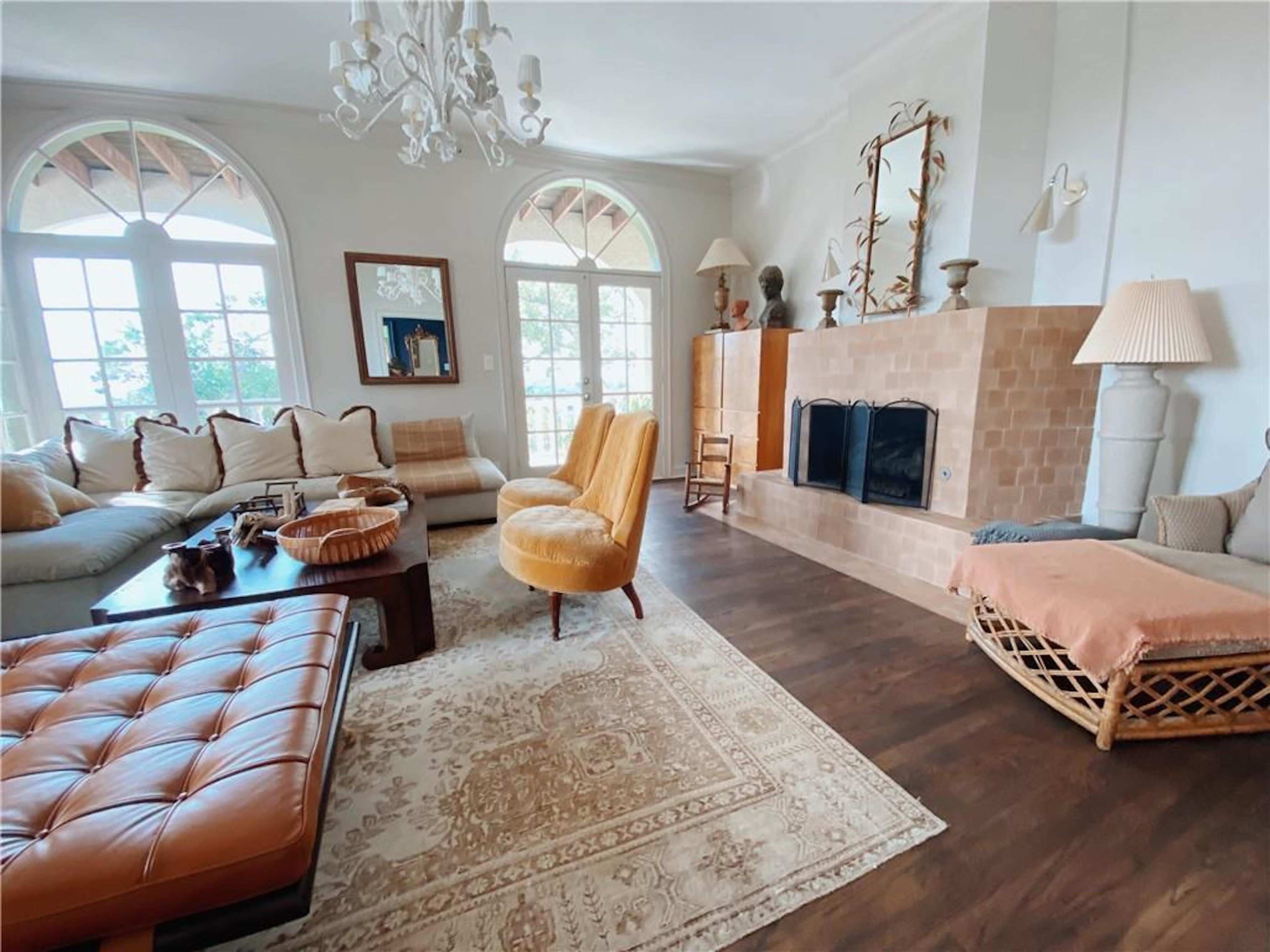 The living room features a large light-colored sectional sofa, two yellow armchairs, and a fireplace with a stone facade, all arranged around a coffee table on a patterned rug.