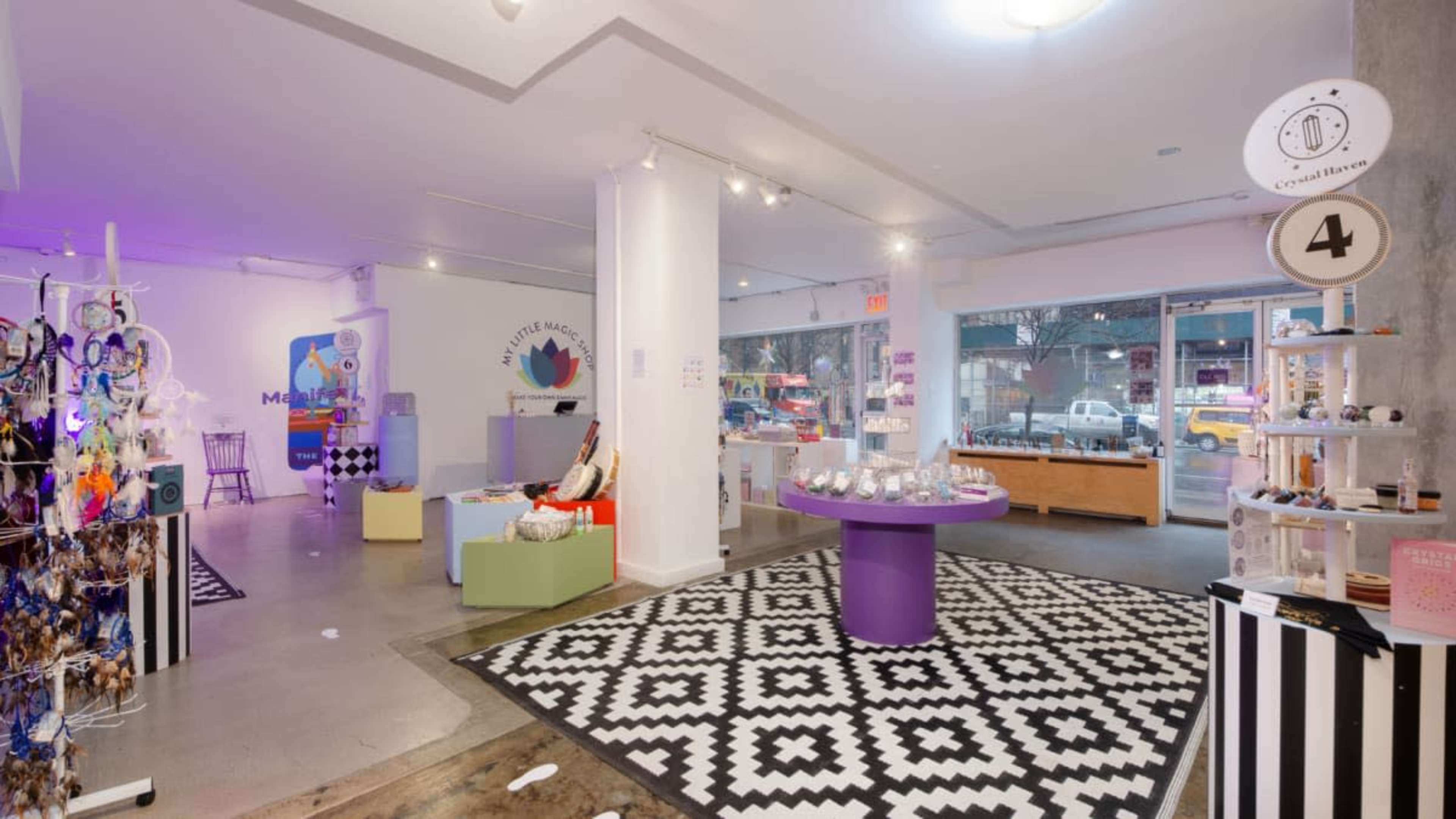 The image shows a brightly lit retail space featuring colorful displays, a patterned black and white rug, and large windows facing the street.