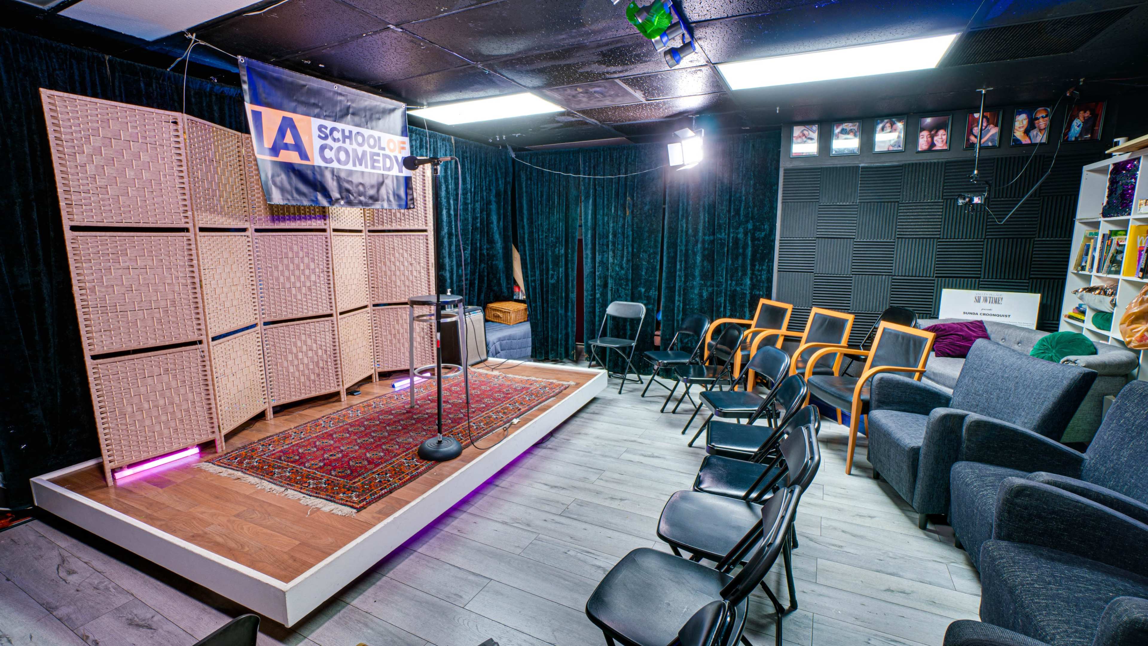 The image shows a comedy performance stage with a microphone stand, surrounded by seating arranged in a semi-circle.