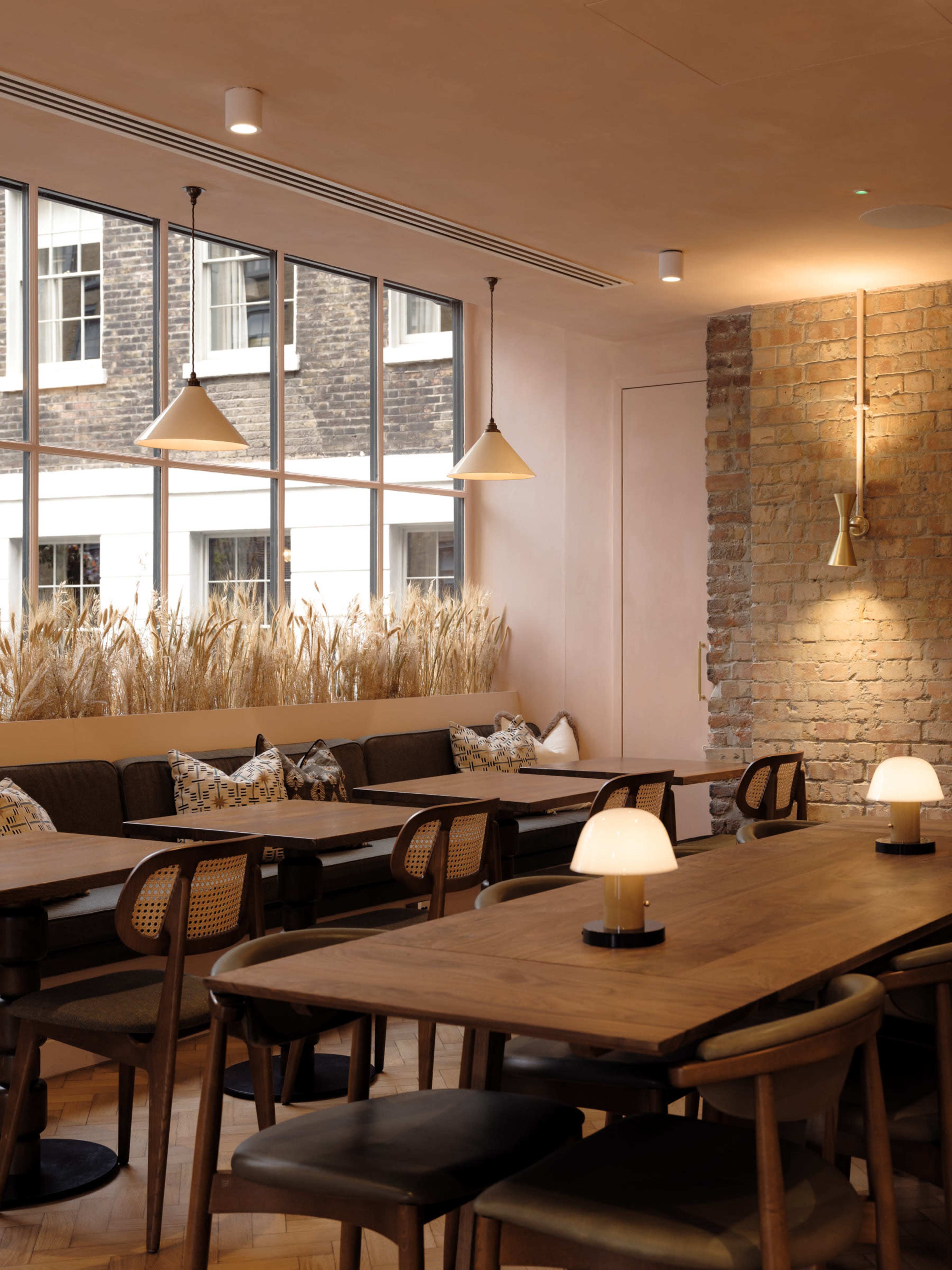 A modern restaurant interior with wooden tables, a cushioned seating area, and large windows illuminated by natural light.