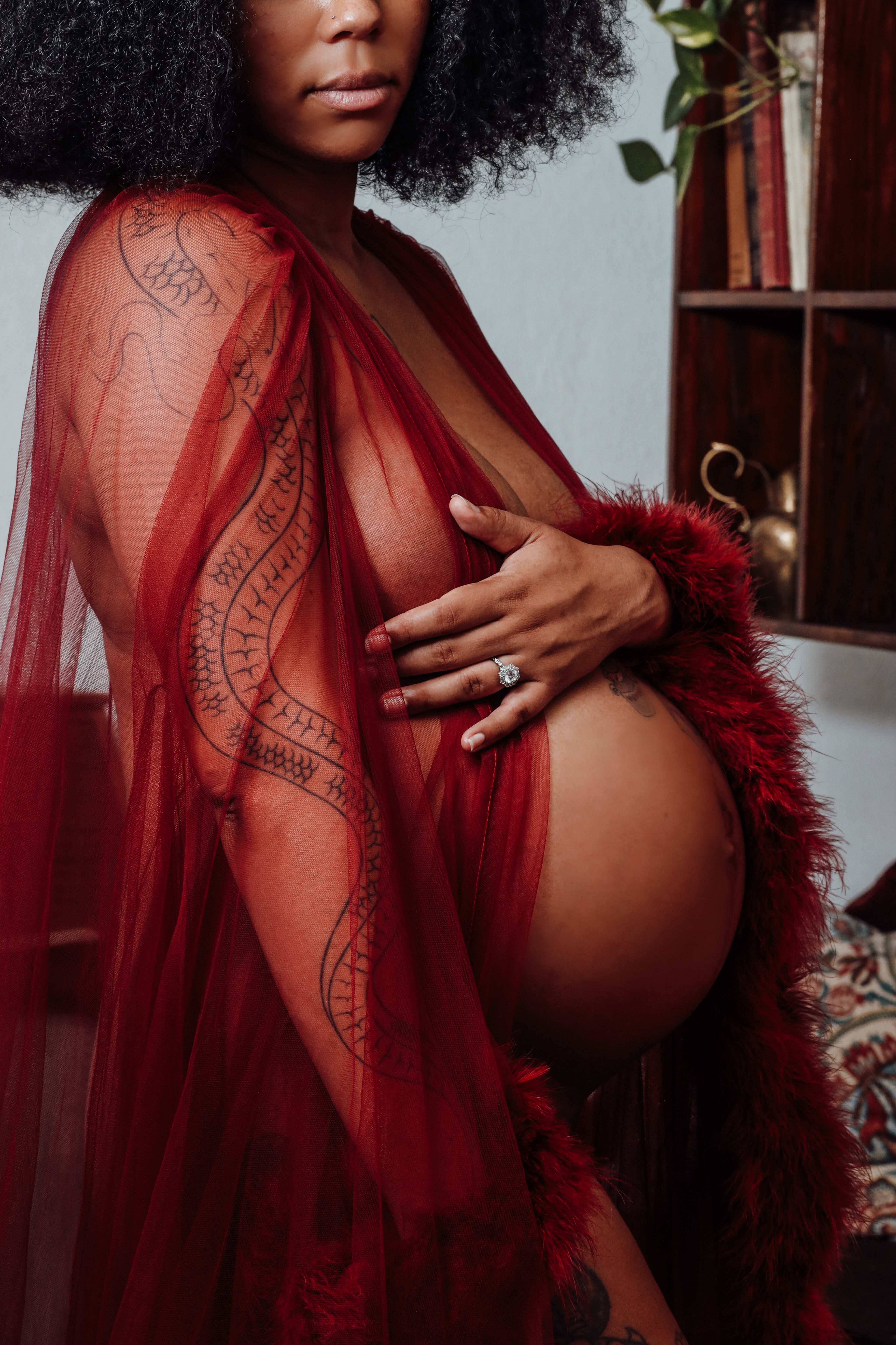 Una mujer con un vestido de maternidad rojo transparente y tatuajes en el cuerpo.