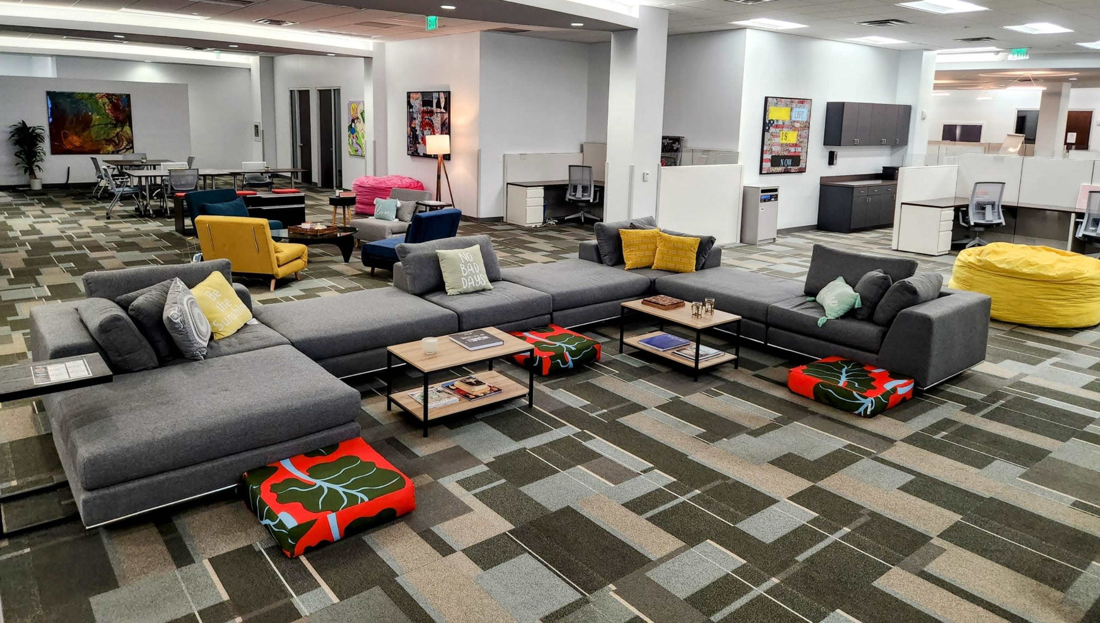 A modern office space featuring a large sectional sofa, colorful bean bags, coffee tables, and workstations in an open layout.