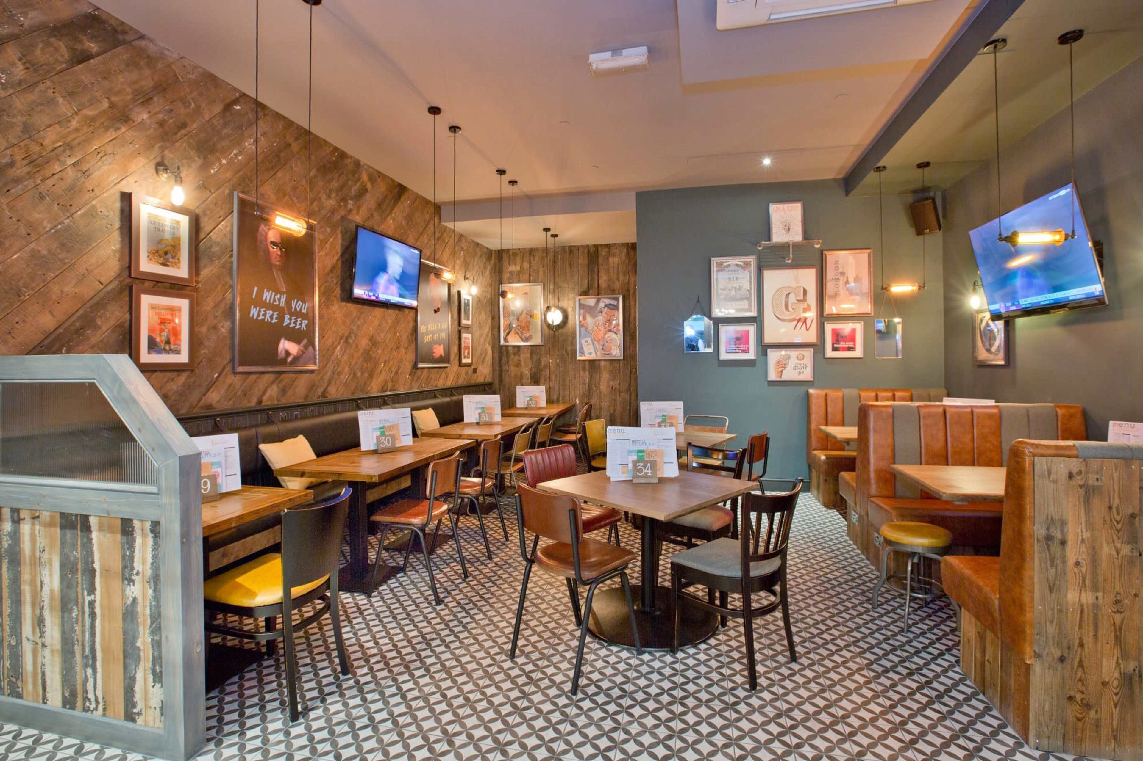 The image shows a cozy restaurant interior featuring wooden walls, patterned flooring, and a mix of seating arrangements with tables and booths.