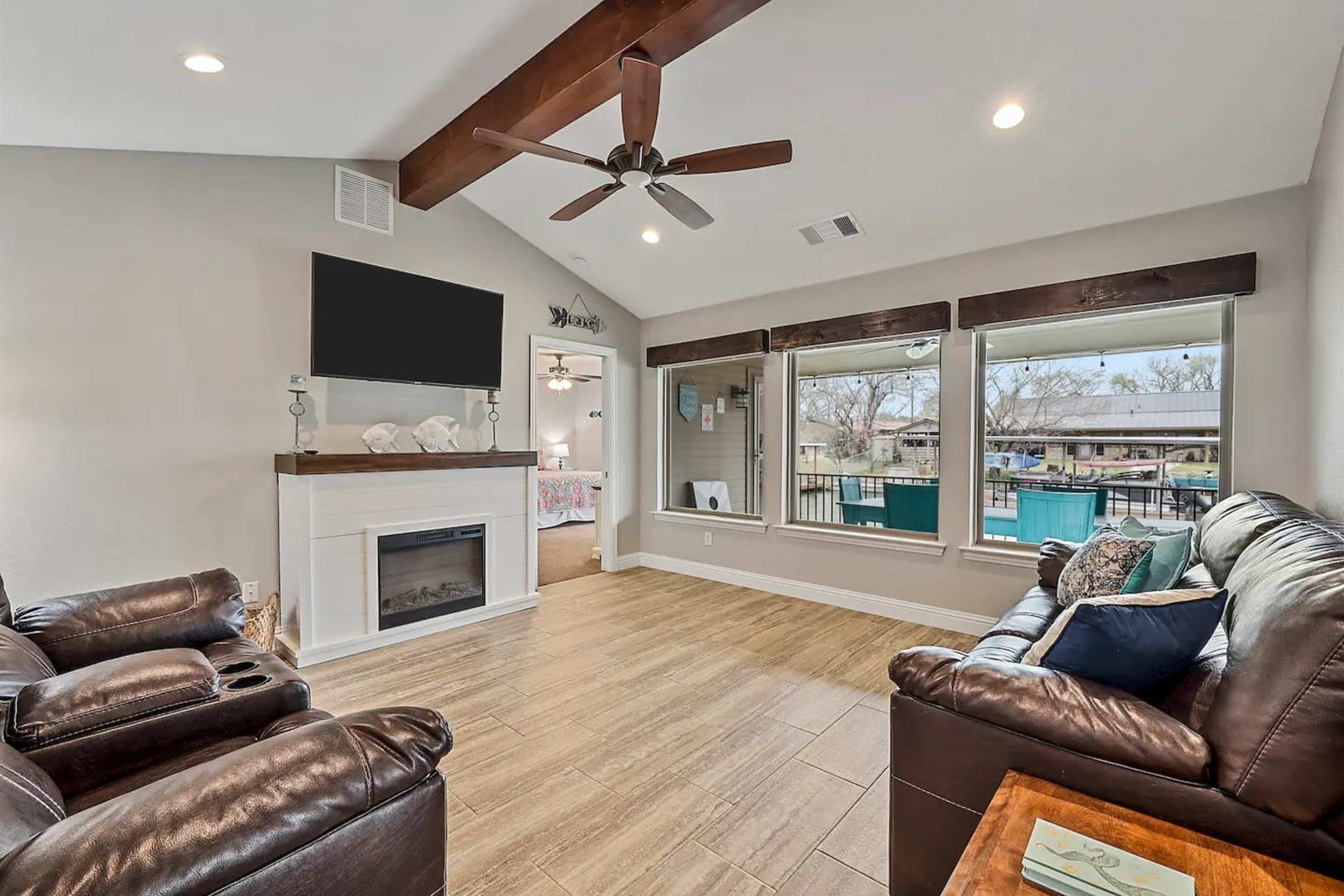 The cozy living room features a leather sofa, a ceiling fan, a wall-mounted television, and large windows that provide a view of the outdoor area.