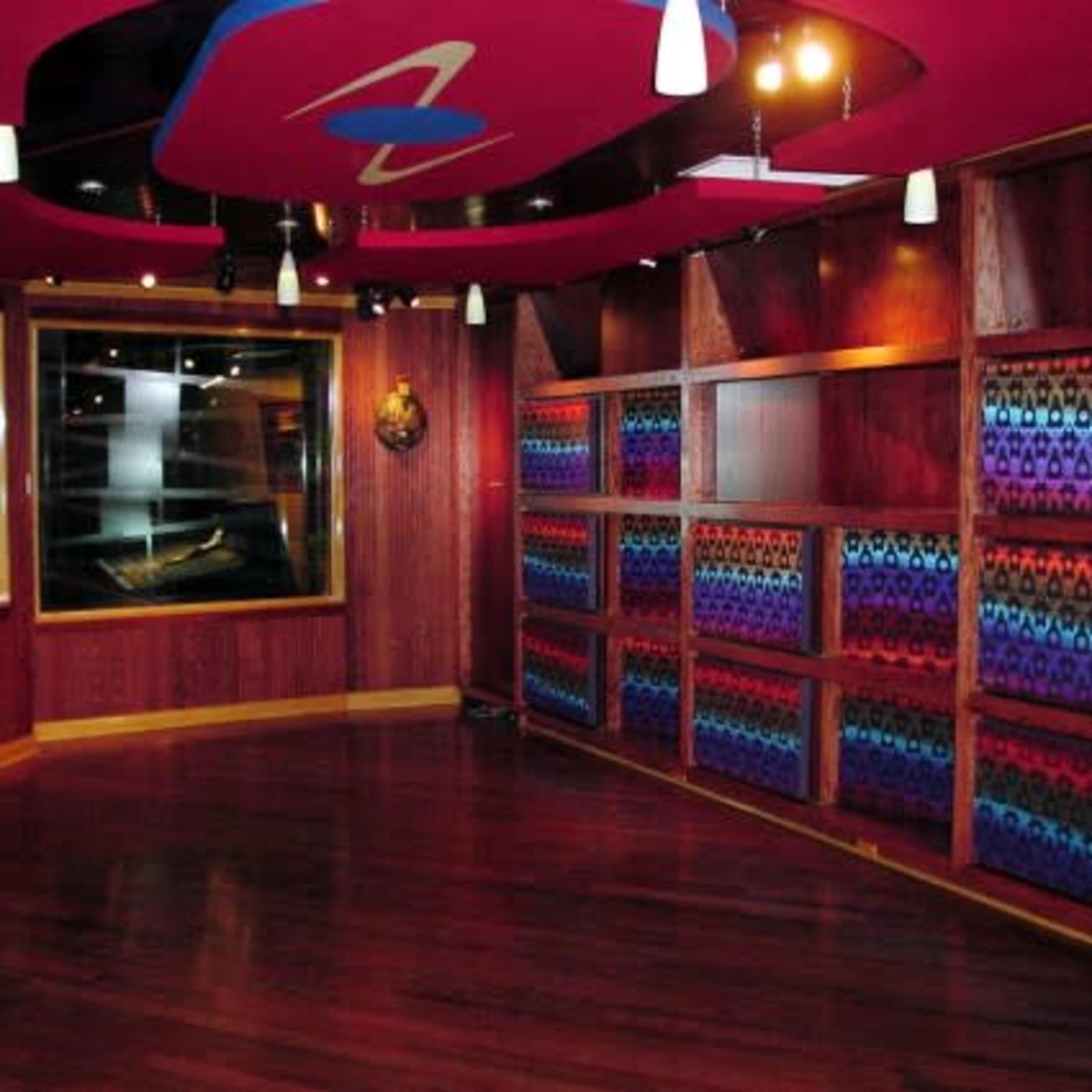 The image shows a modern interior room with wooden shelves displaying colorful patterned fabric or materials, illuminated by overhead lights.