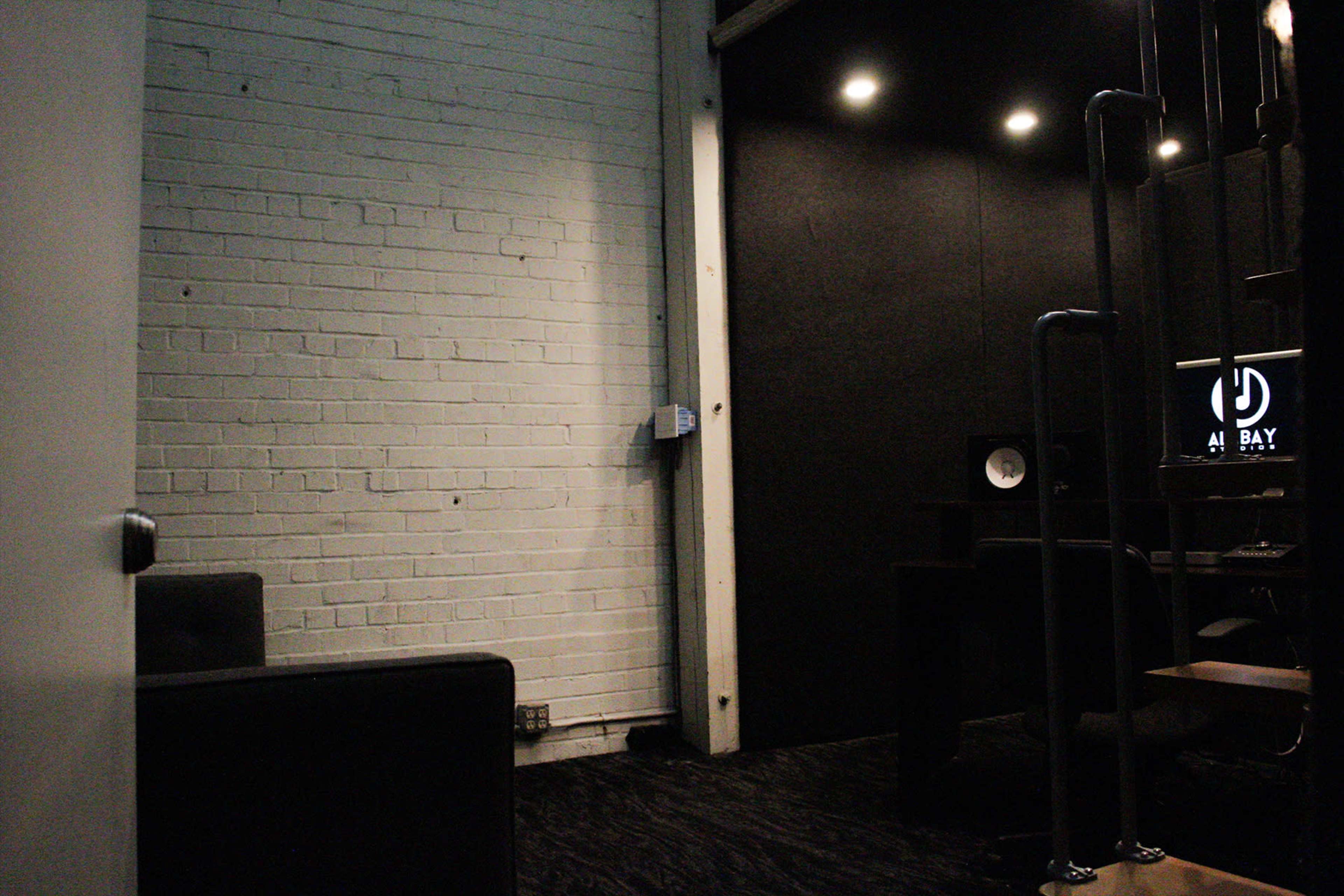 A minimalistic room with a white brick wall, a dark fabric wall, and a computer setup in a corner.