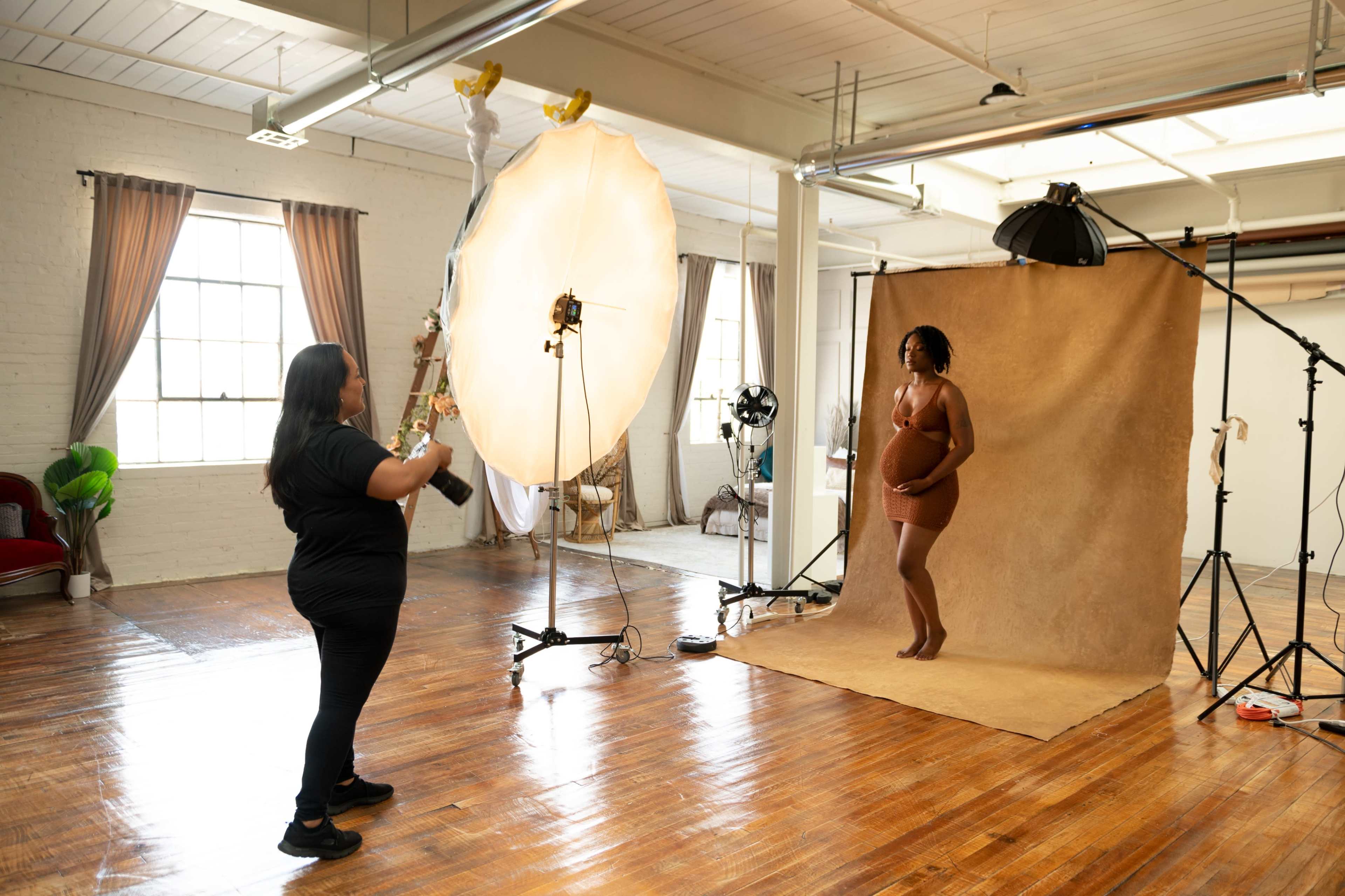 A photographer captures a model posed with a large round prop in a studio setting with soft lighting and backdrops.