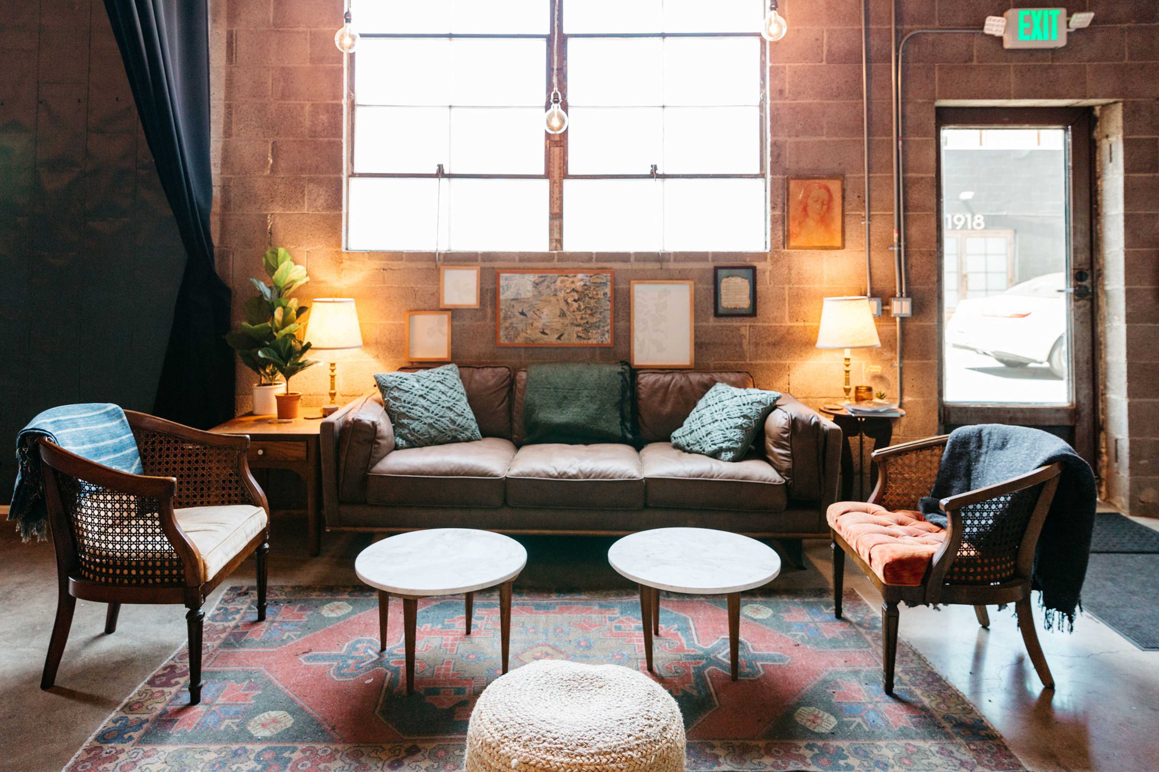 A cozy living area with a brown leather sofa, two armchairs, and three coffee tables arranged on a patterned rug under large windows.