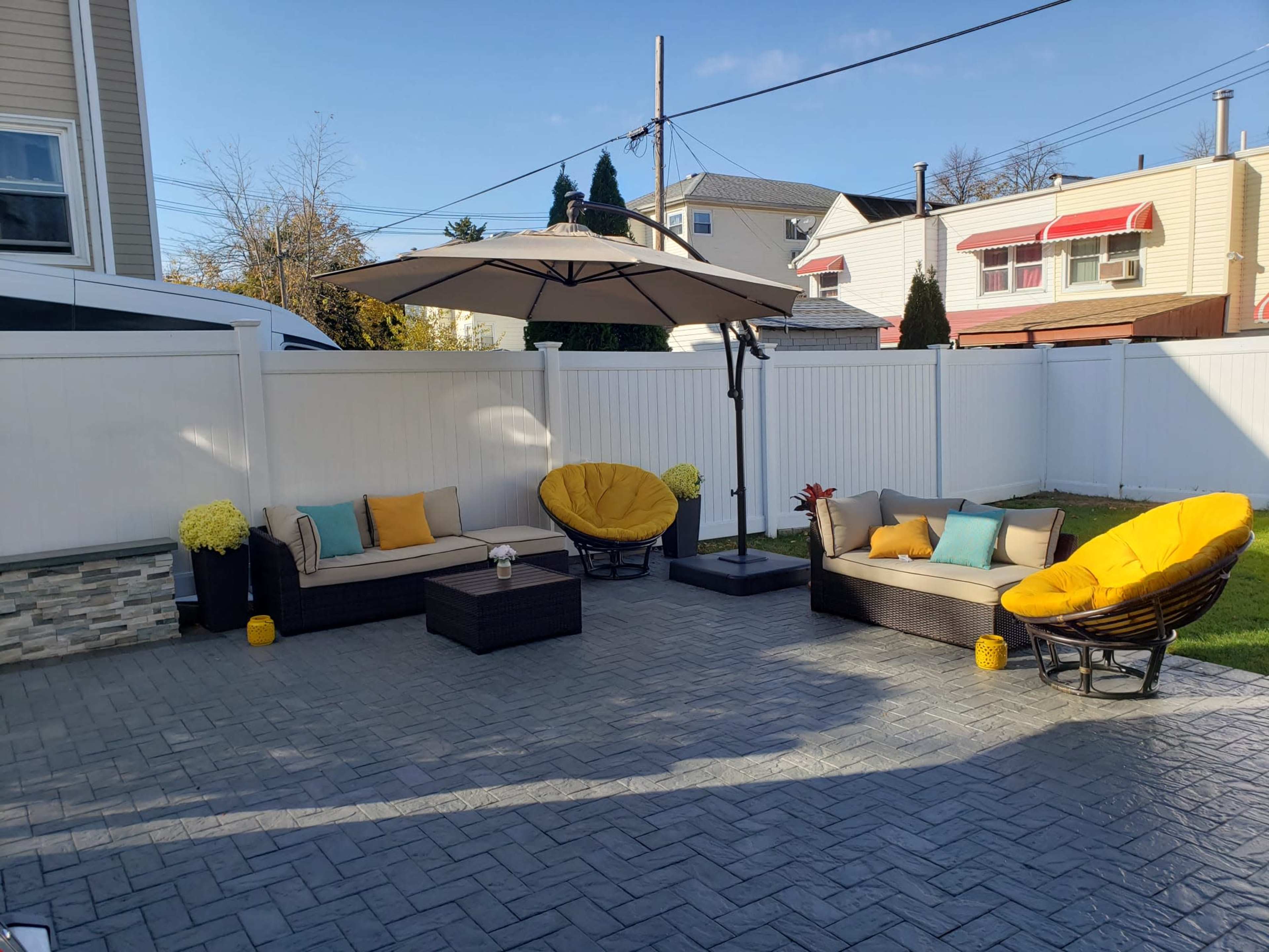 A patio area features two round chairs, a sofa, a coffee table, and an umbrella, all surrounded by a white fence.