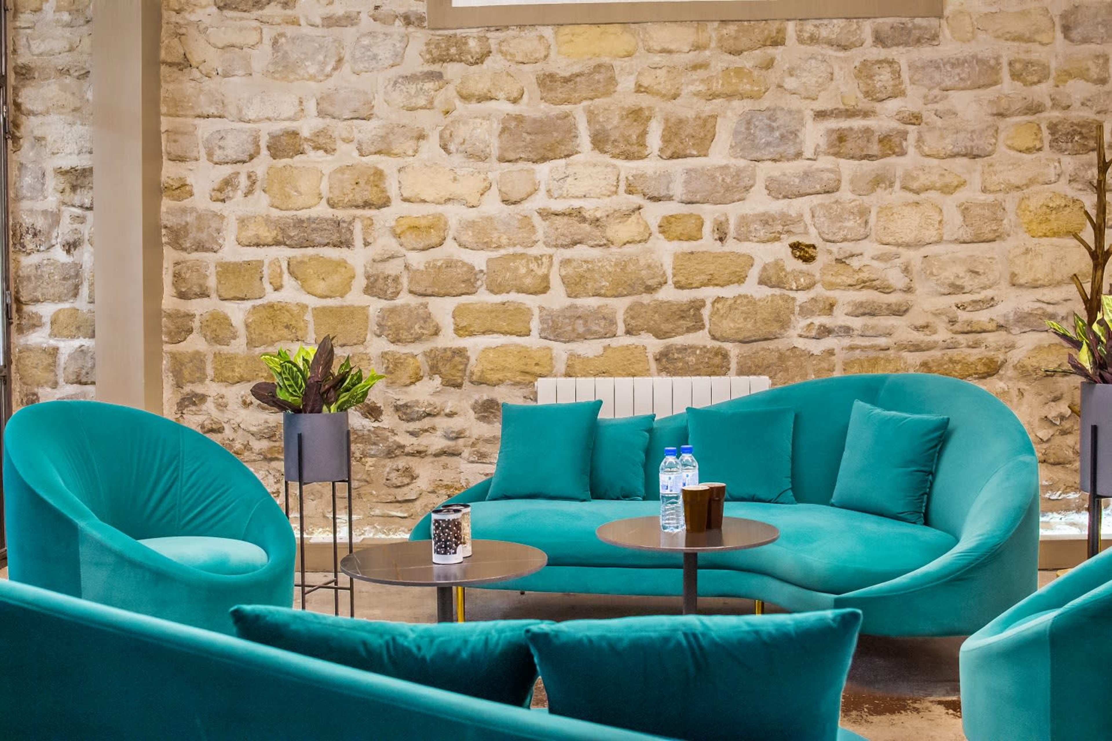 A cozy seating area with turquoise sofas and tables set against a textured stone wall.