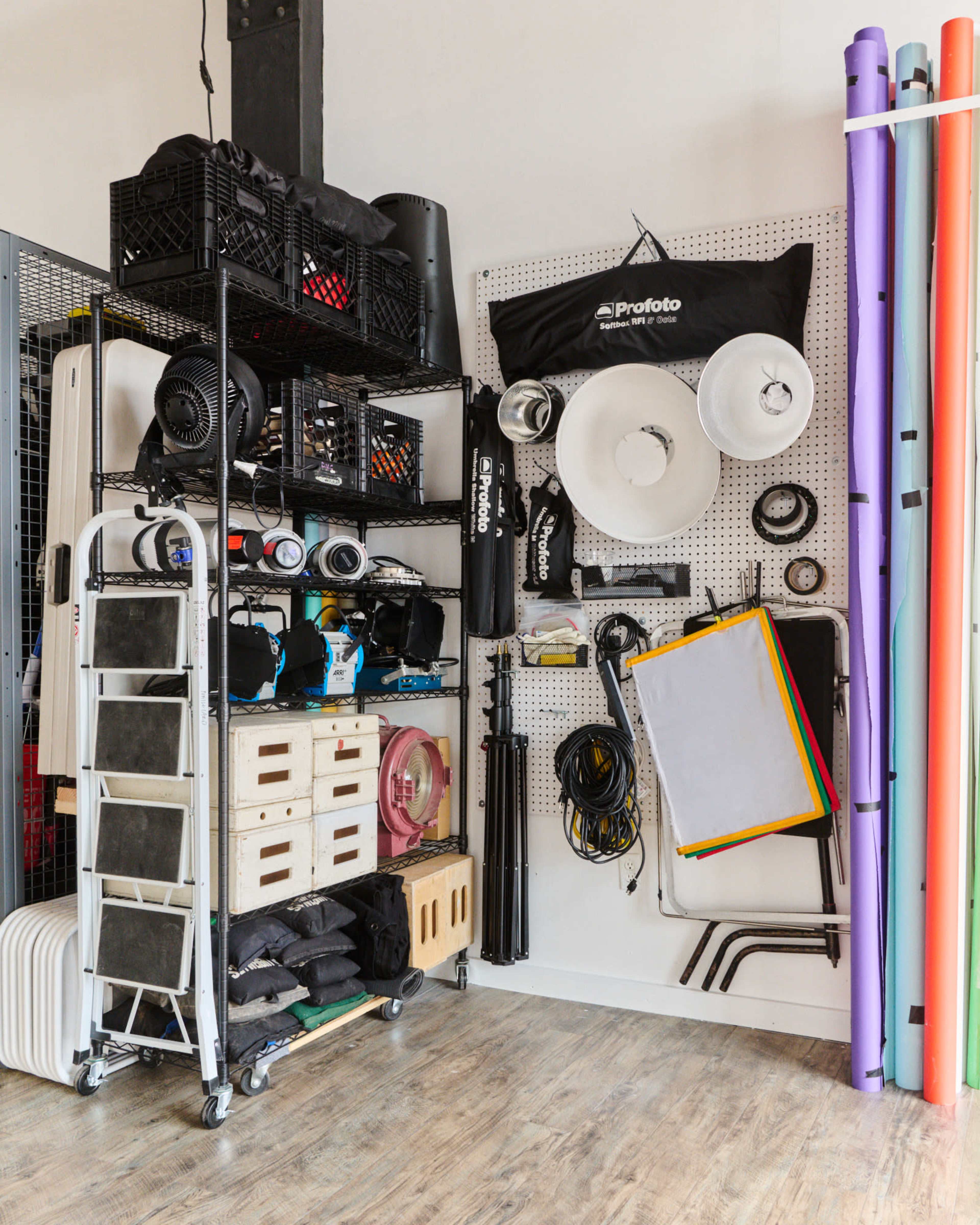 A neatly organized storage area with various photography equipment and accessories arranged on shelves and a ladder against a wall.