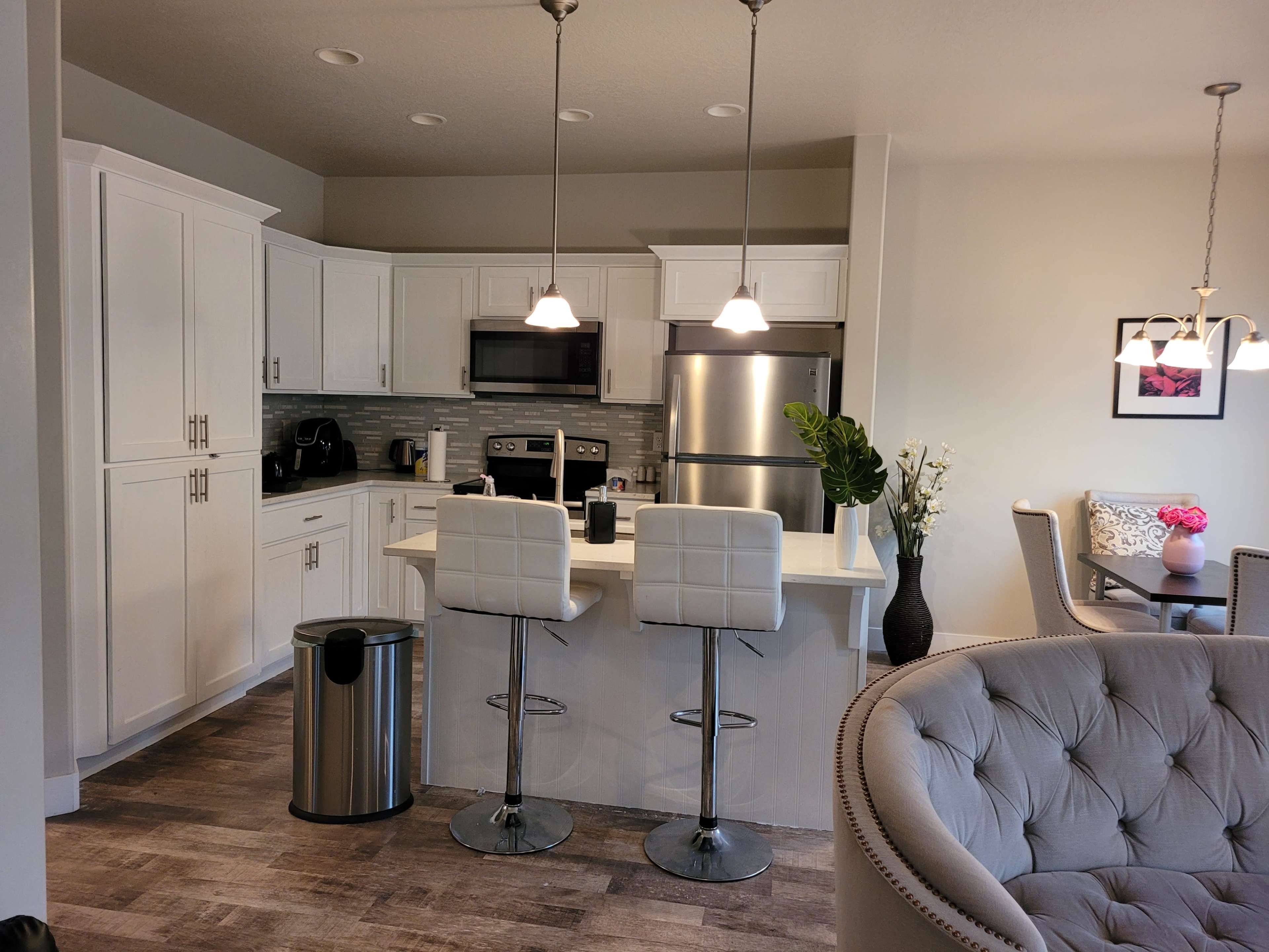 A modern kitchen with white cabinets, stainless steel appliances, and a breakfast bar with two stools.