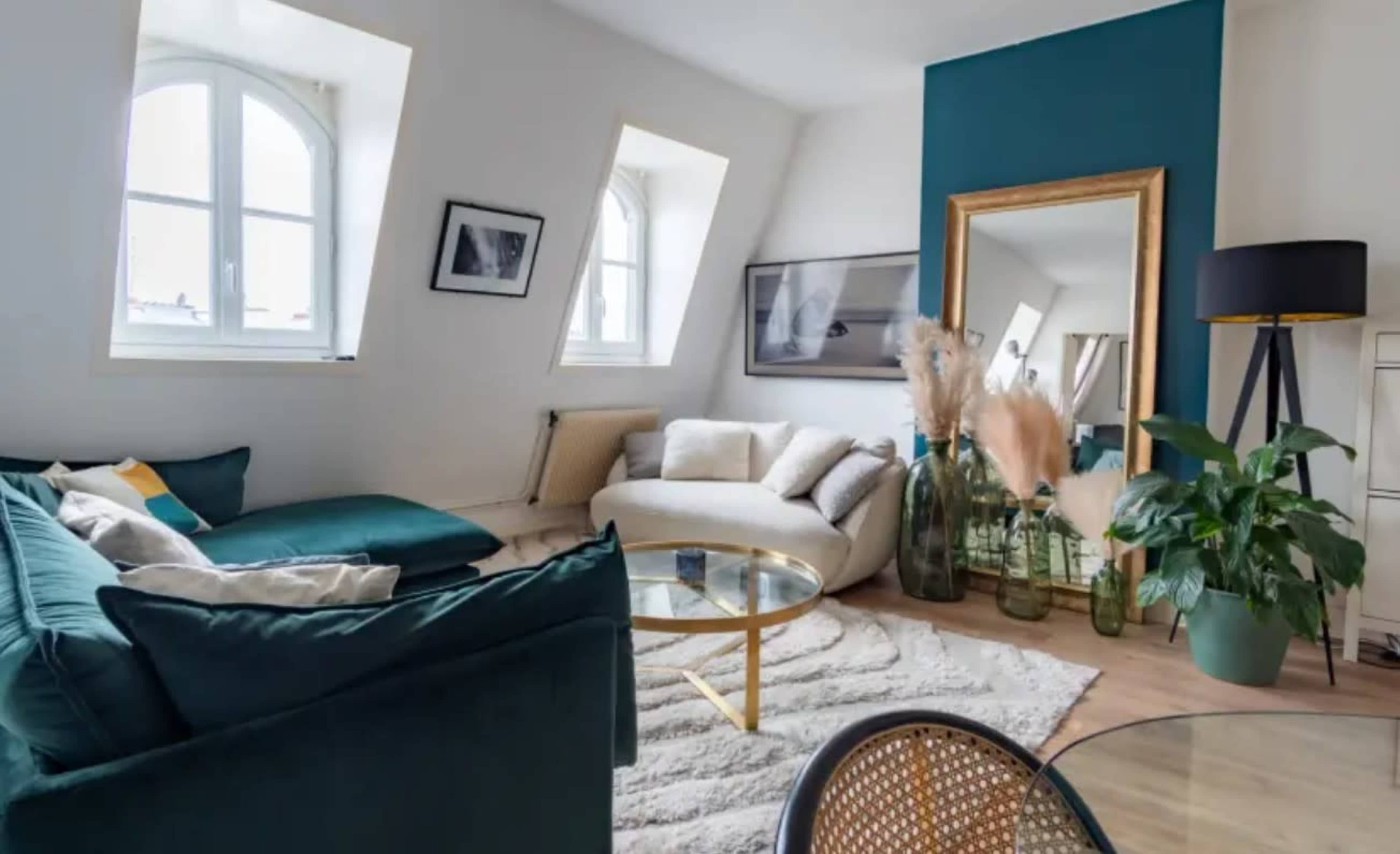 The image showcases a modern living room featuring a curved white sofa, a round glass coffee table, and decorative plants, with a large mirror and artwork on the walls.