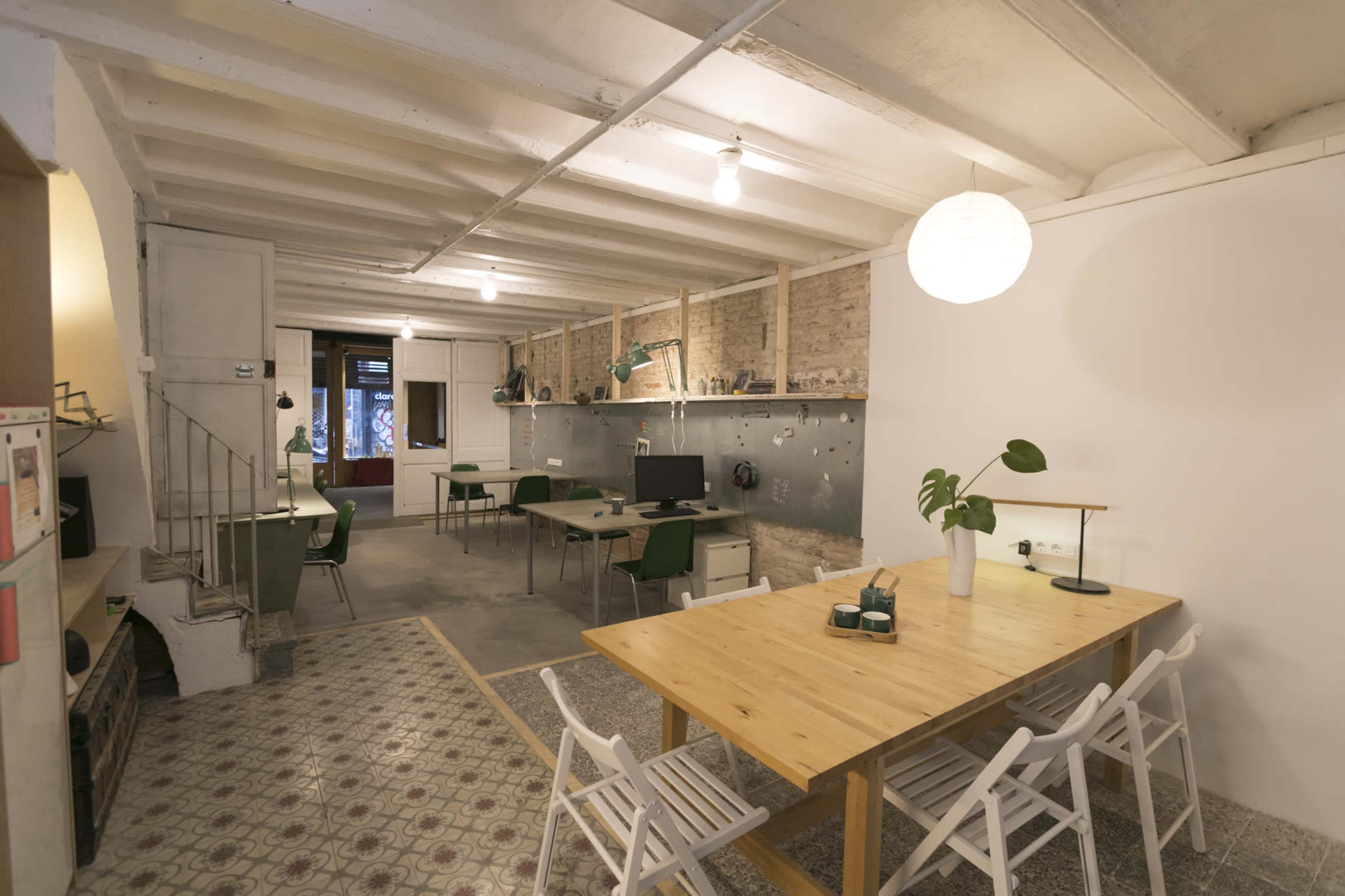 A spacious room with a dining area featuring wooden tables and chairs, a workspace with computers, and a minimalist design aesthetic.