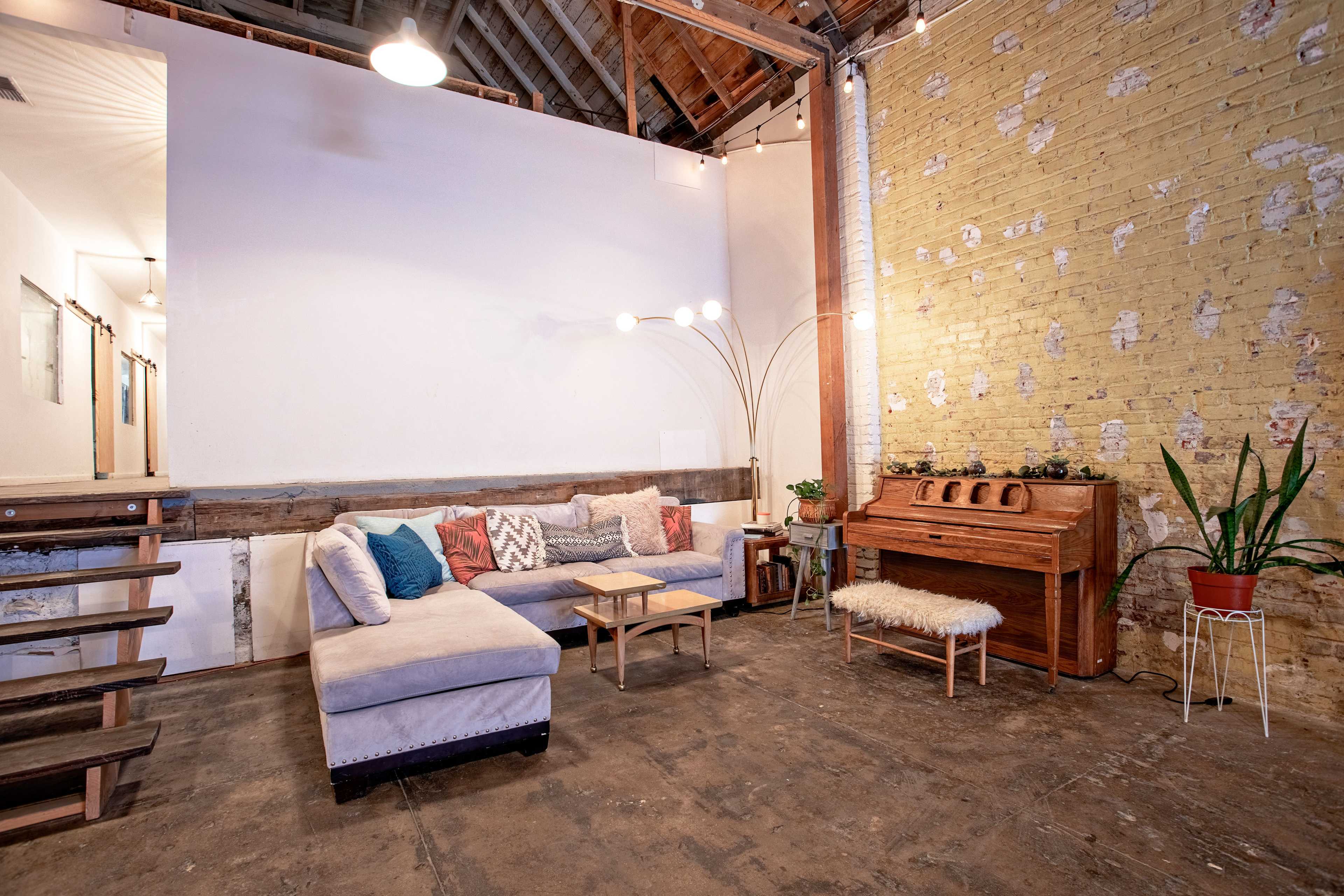 A spacious living area featuring a sectional sofa, a wooden console, a plant, and exposed brick walls with a rustic finish.
