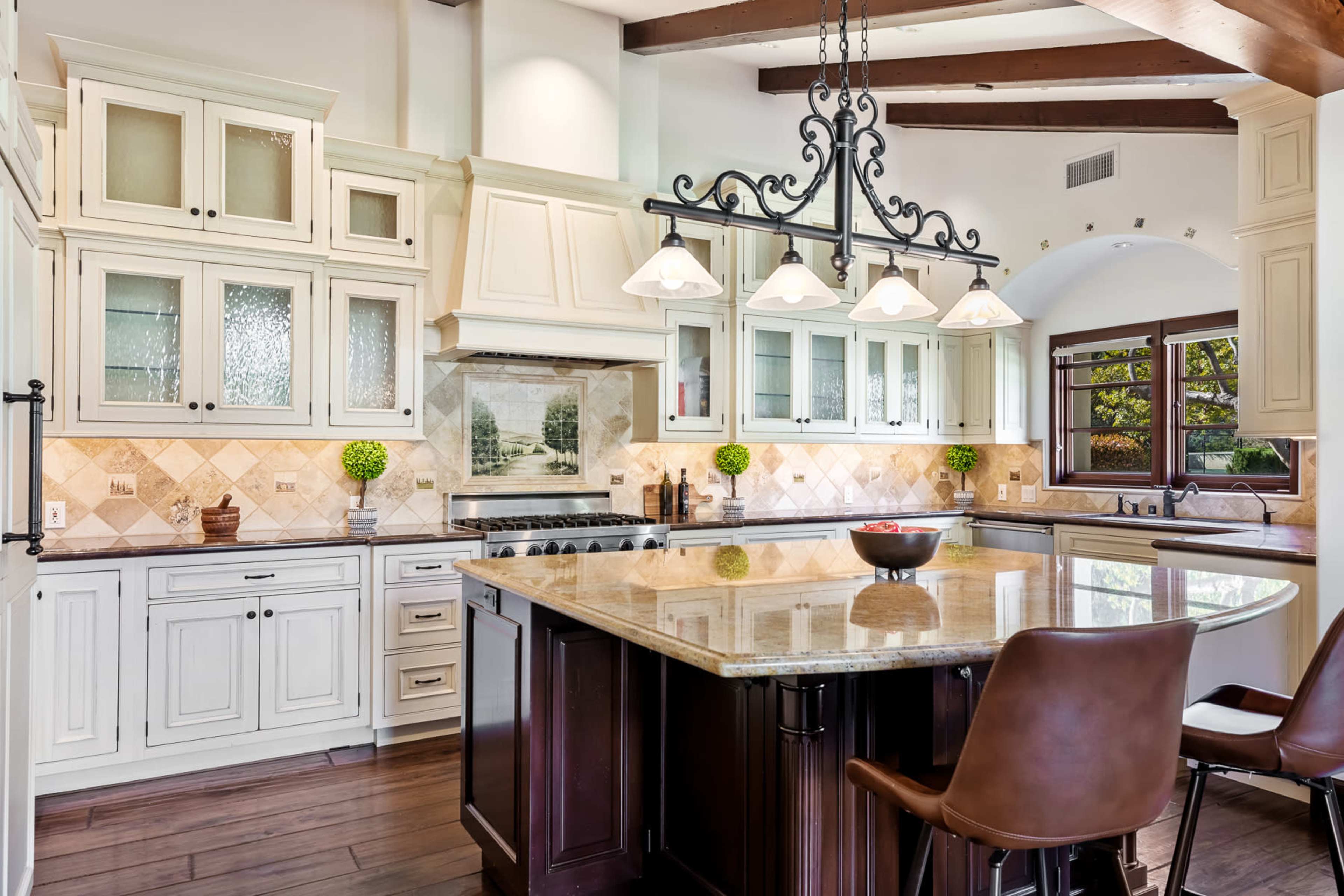 The image shows a spacious kitchen featuring white cabinets, a large granite island, and hanging pendant lights over the eating area.
