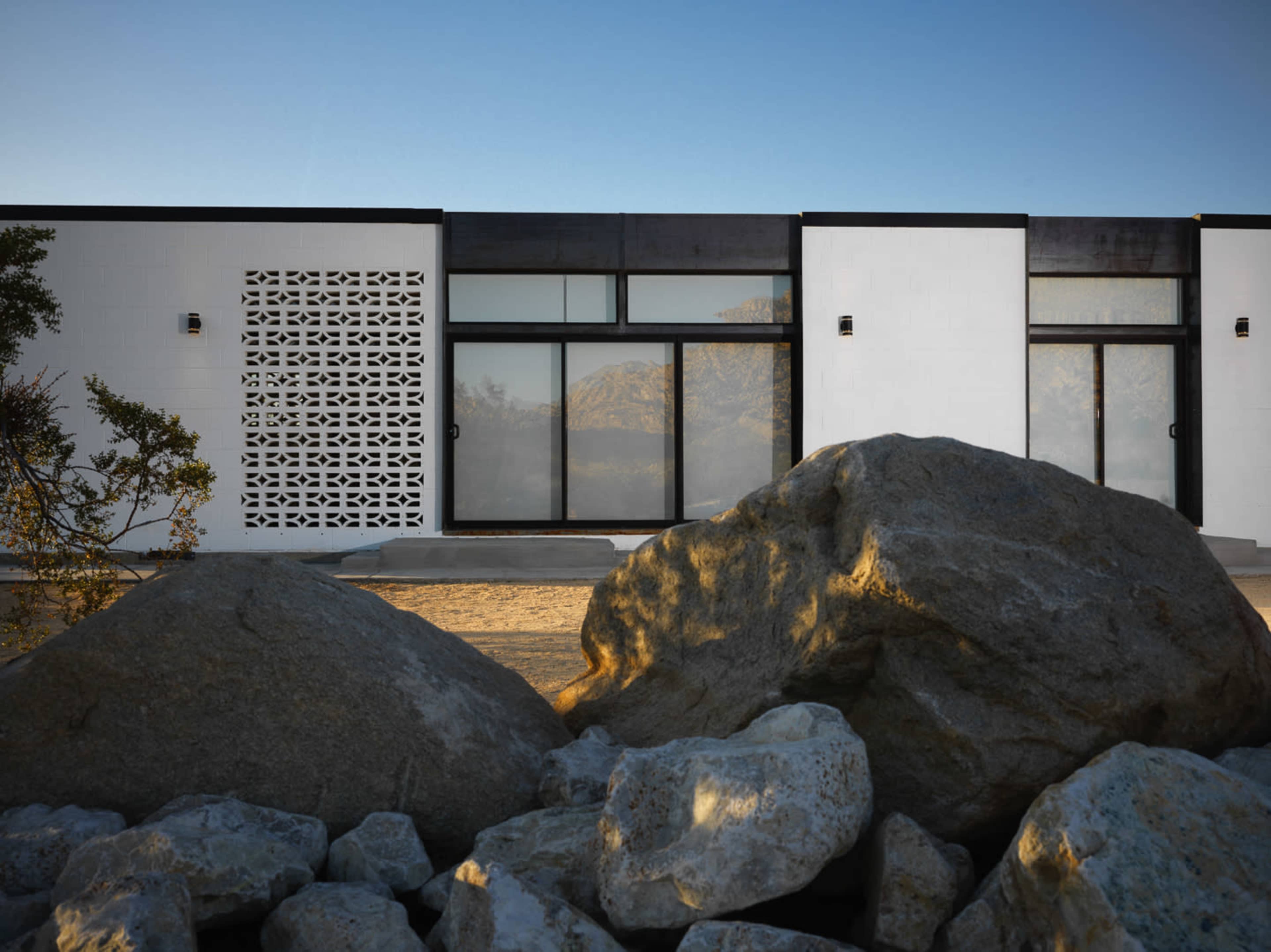 A modern building with large windows and a decorative wall panel stands in front of large boulders under a clear sky.