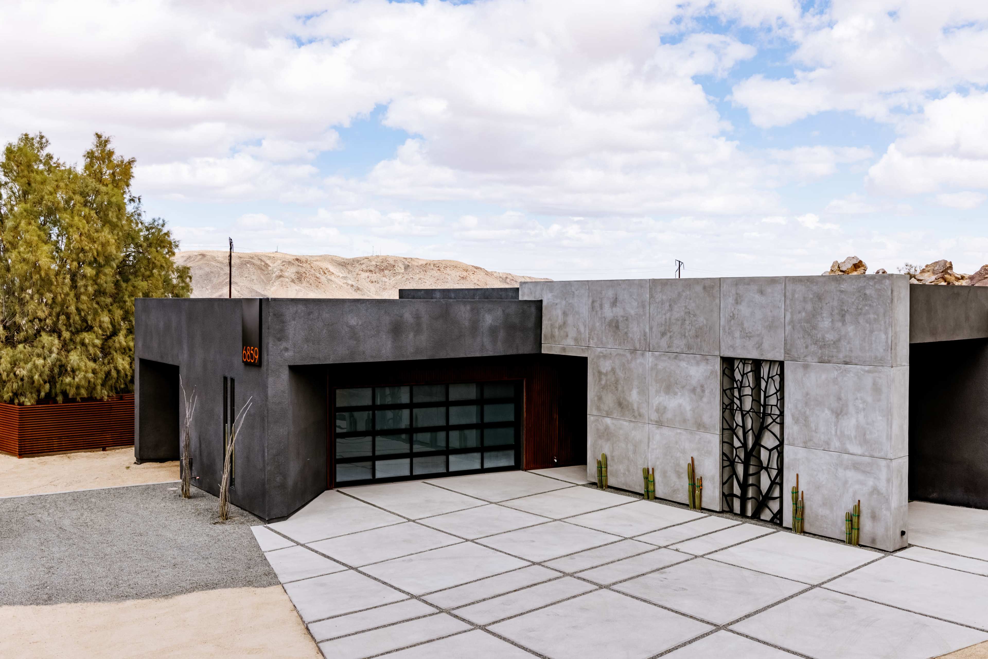 A modern house featuring a combination of black and gray concrete exteriors, surrounded by a desert landscape.