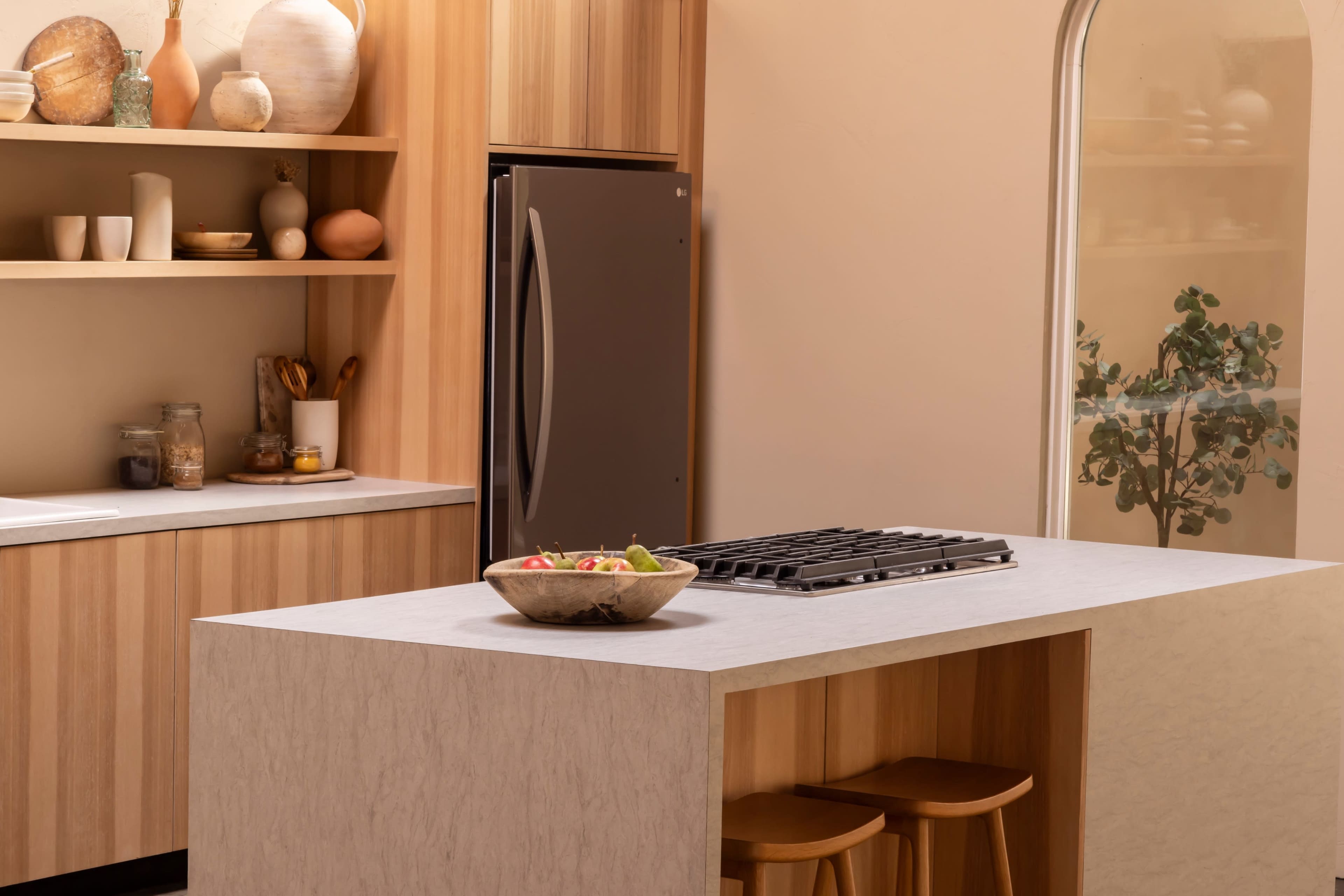 The image shows a modern kitchen featuring a marble countertop island with a gas stove, wooden cabinetry, and a large refrigerator.