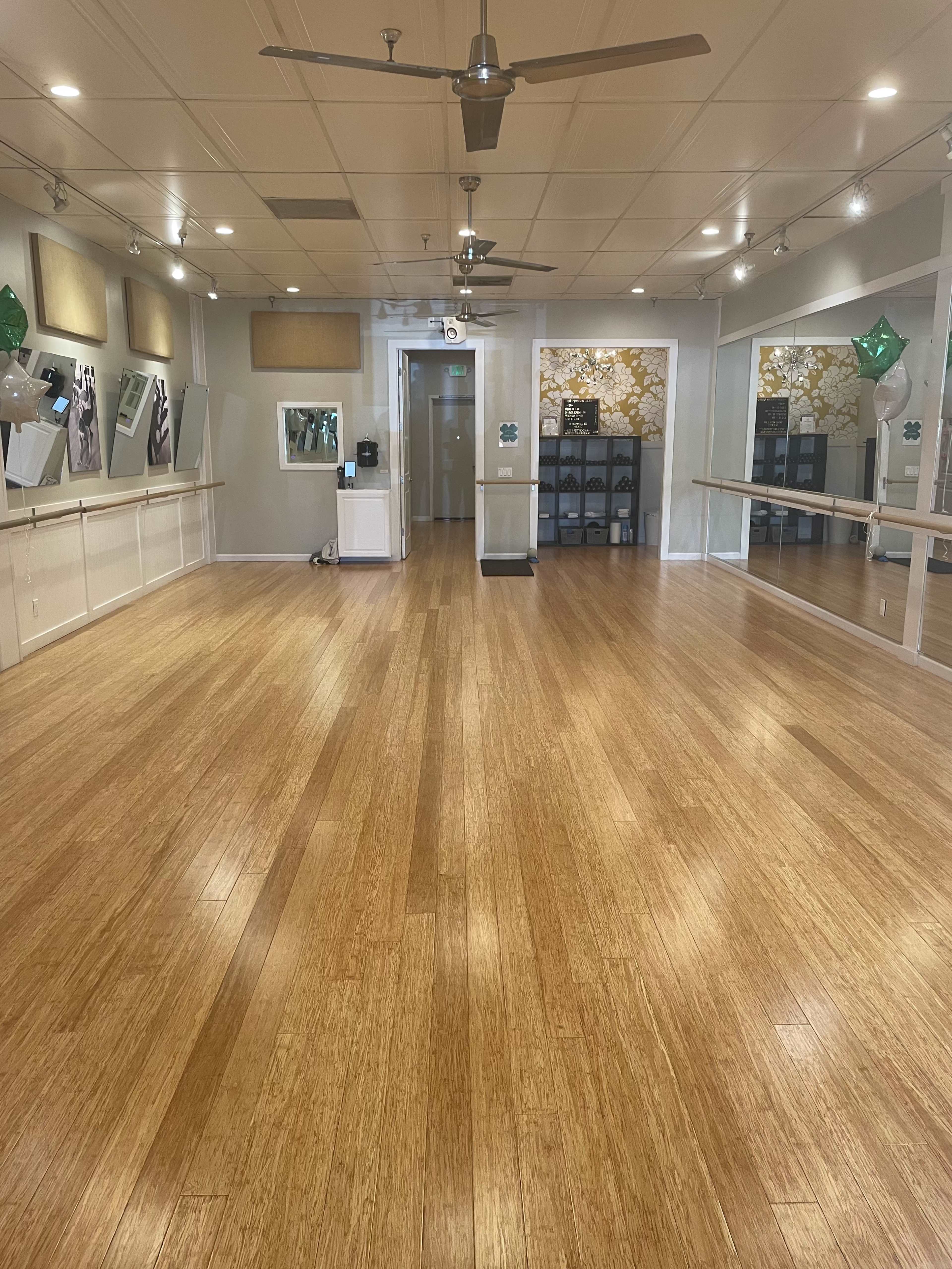 A spacious dance studio with wooden flooring, large mirrors, and bright lighting.