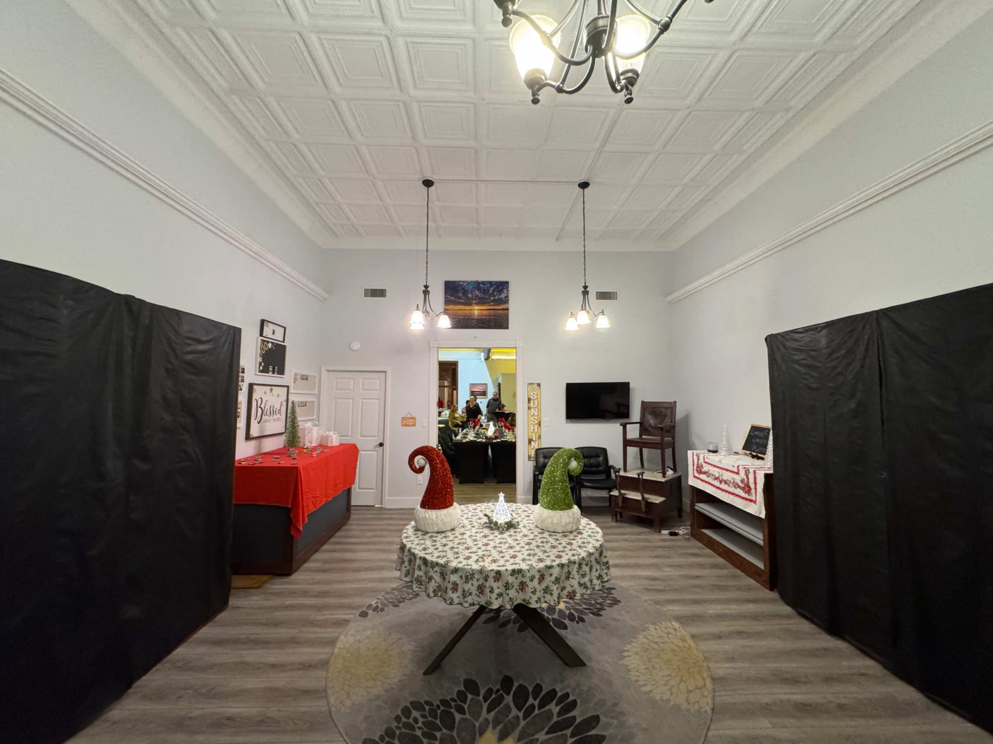 The room features a circular table with a decorative tablecloth and festive elements, surrounded by black curtains and adorned with Christmas decorations.