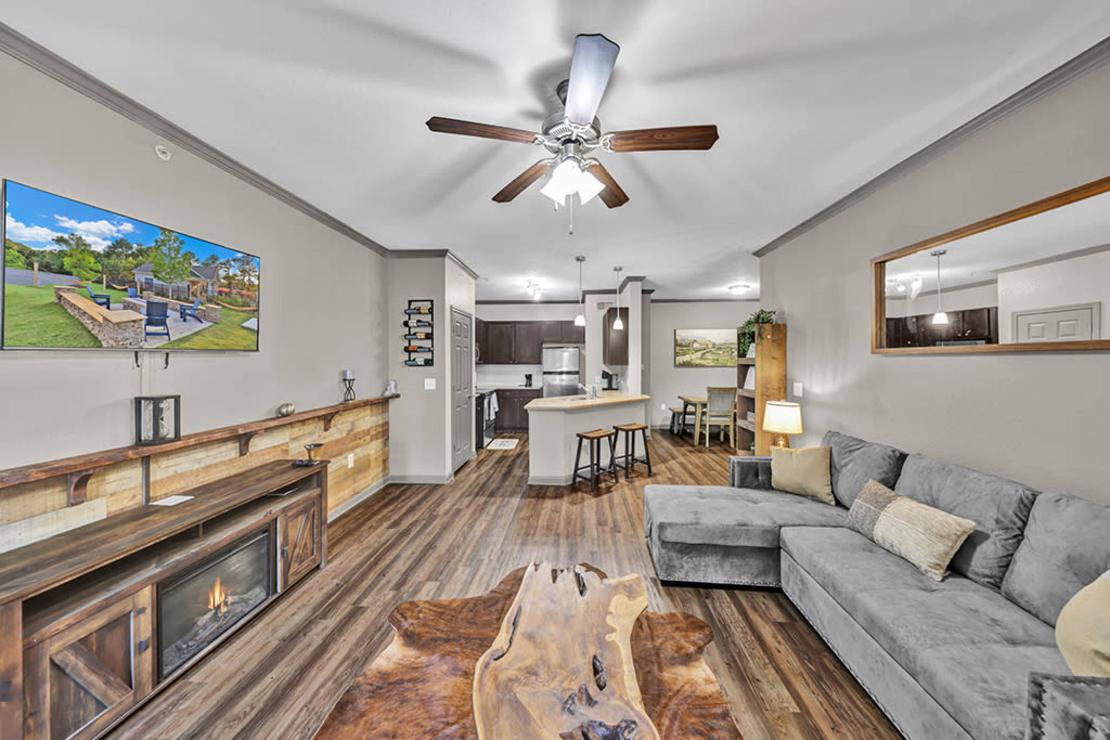 A modern living room with a gray sofa, wooden coffee table, and a television mounted on the wall, adjacent to an open kitchen area.