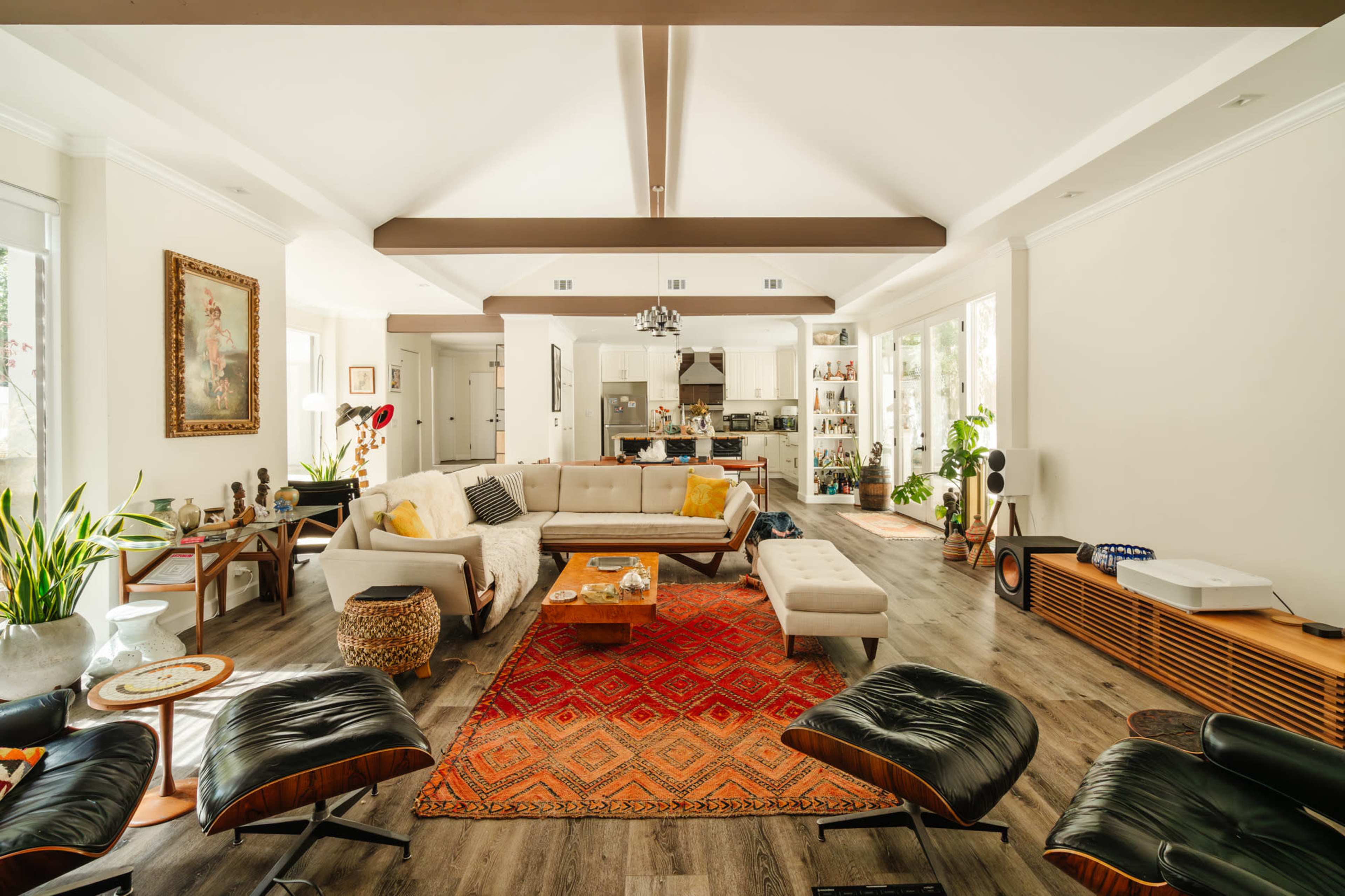 The spacious living room features a sectional sofa, an area rug, several lounge chairs, a coffee table, and a kitchen visible in the background.