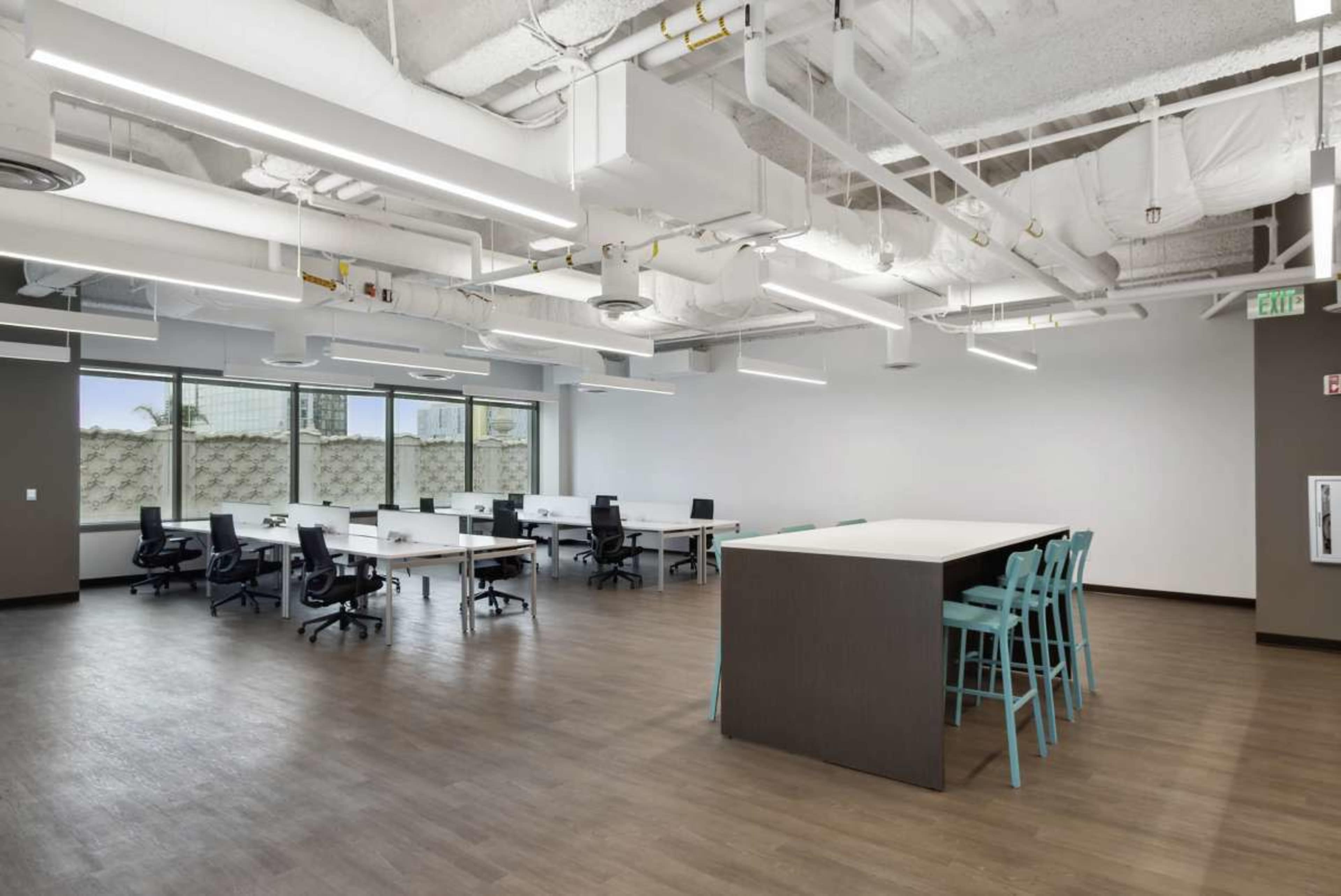 A modern office space with several desks, chairs, and a seating area featuring teal bar stools around a counter.