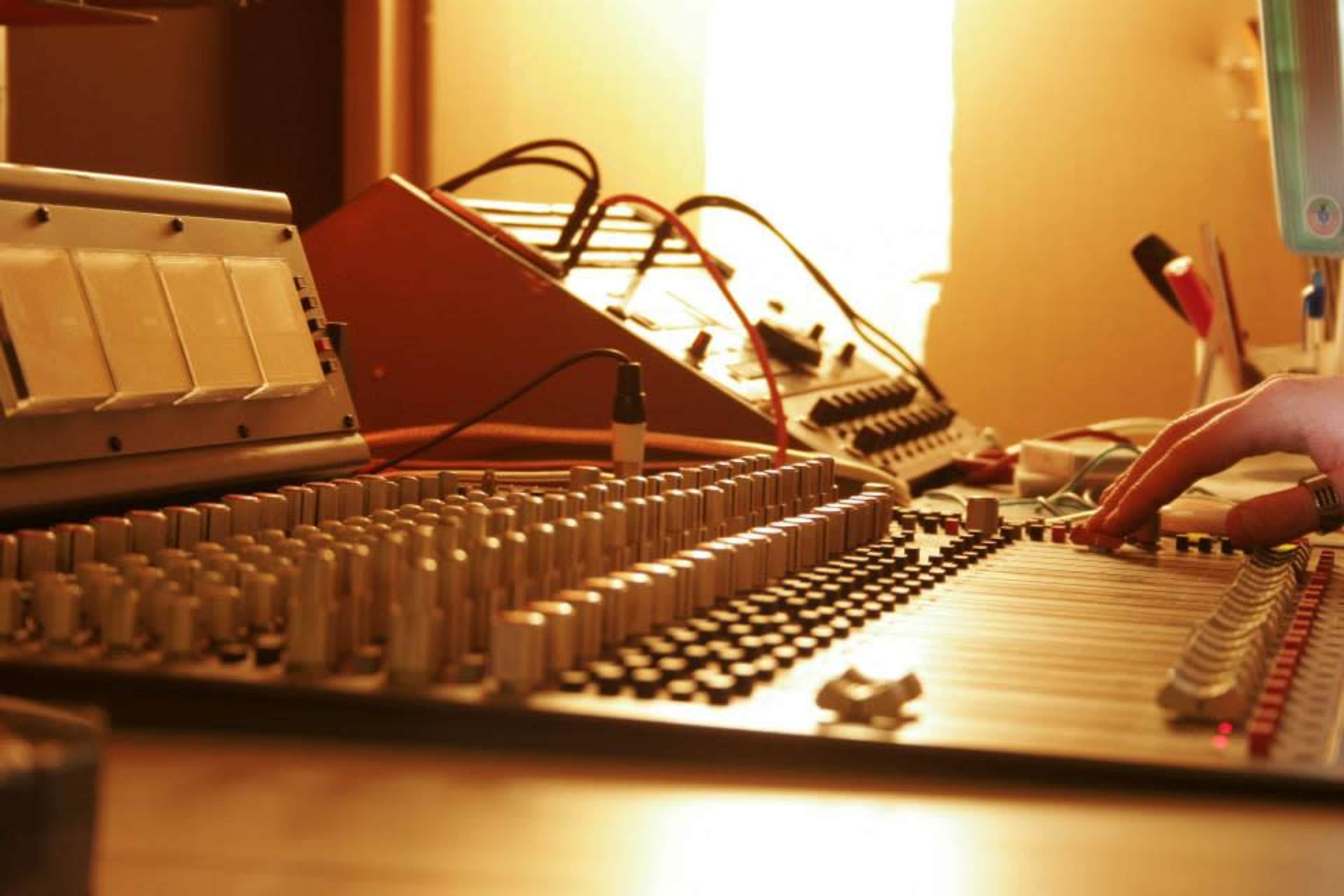 A close-up view of a sound mixing console with various knobs and sliders, and a hand adjusting the controls.