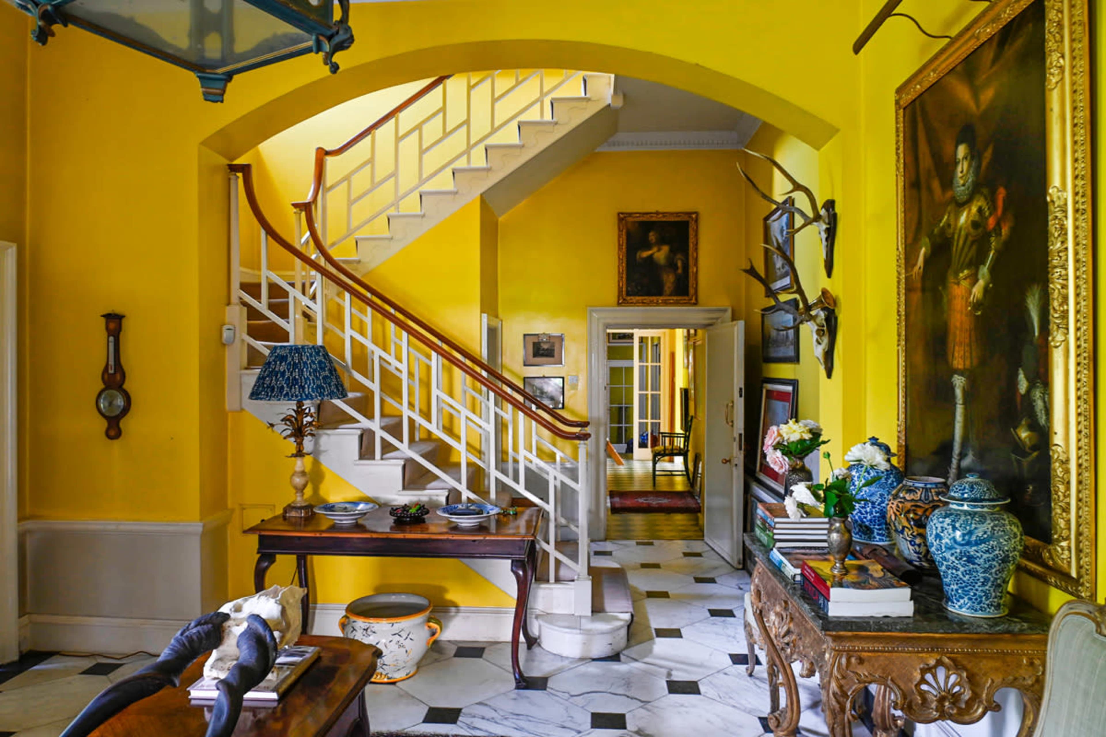 A bright yellow hallway featuring a staircase, a console table with decorative items, and artwork on the walls.