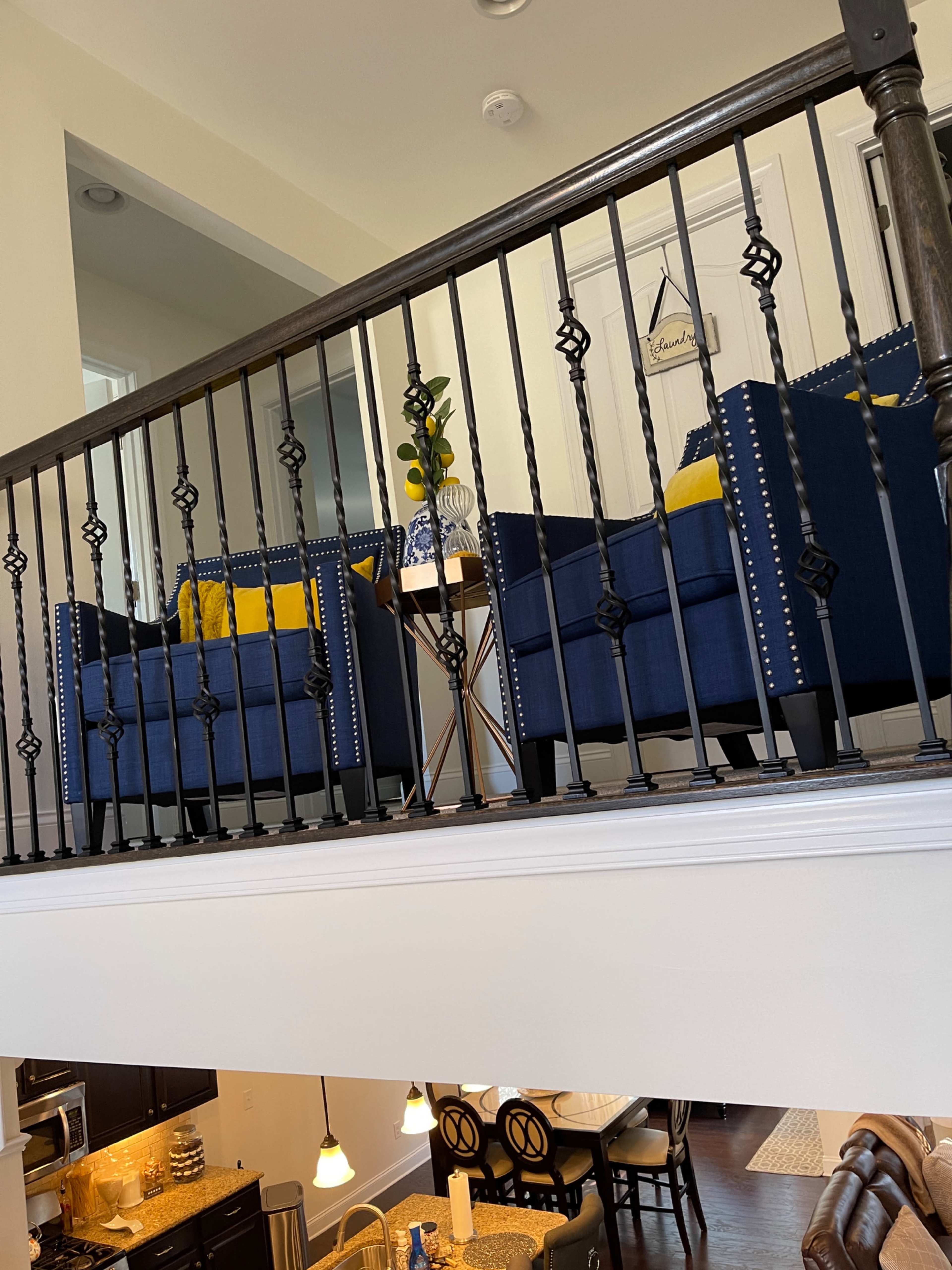 A loft area with two blue armchairs and a small table, overlooking a dining area below.