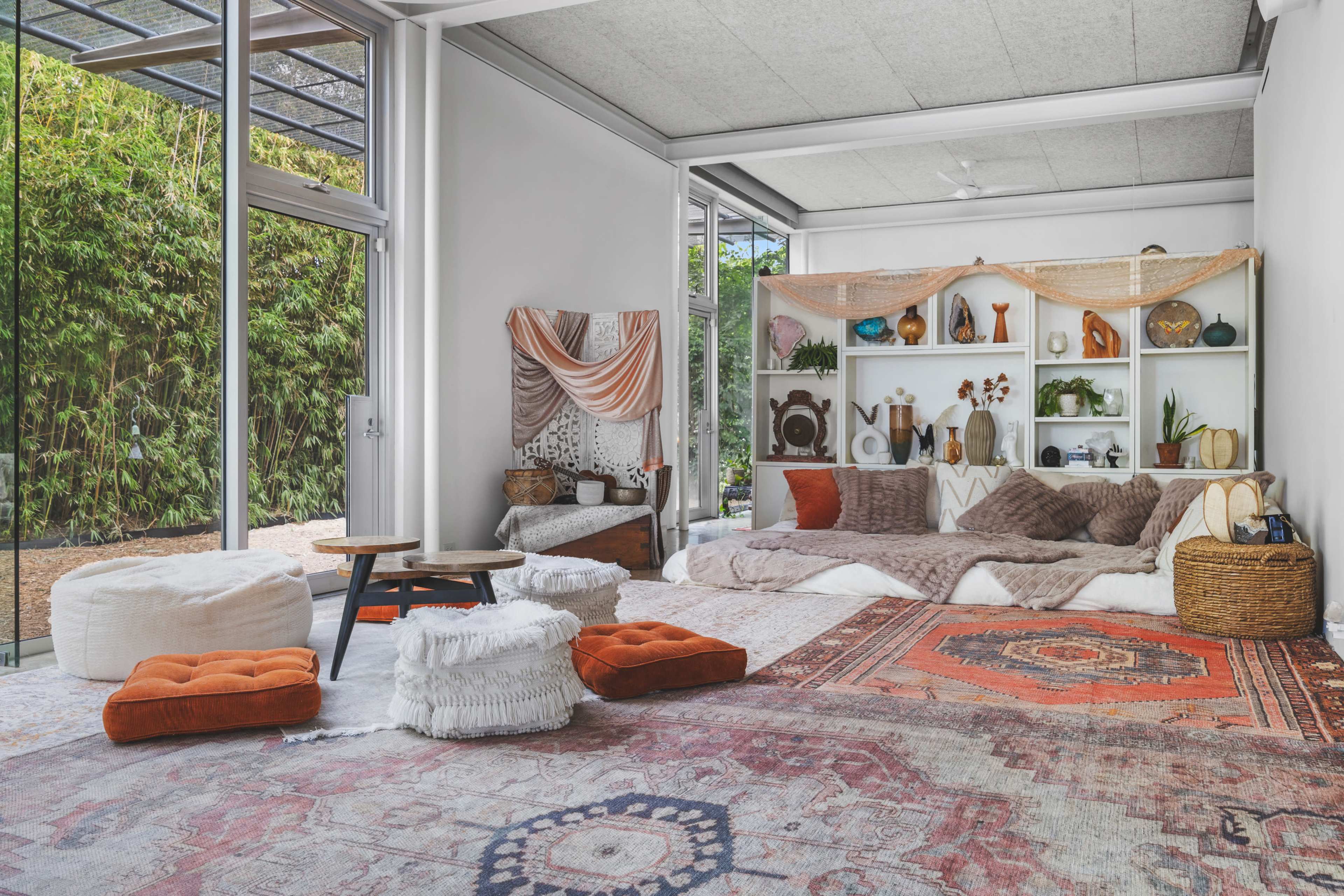 A spacious living area features a large seating arrangement with cushions and rugs, surrounded by shelves displaying decorative items and plants.