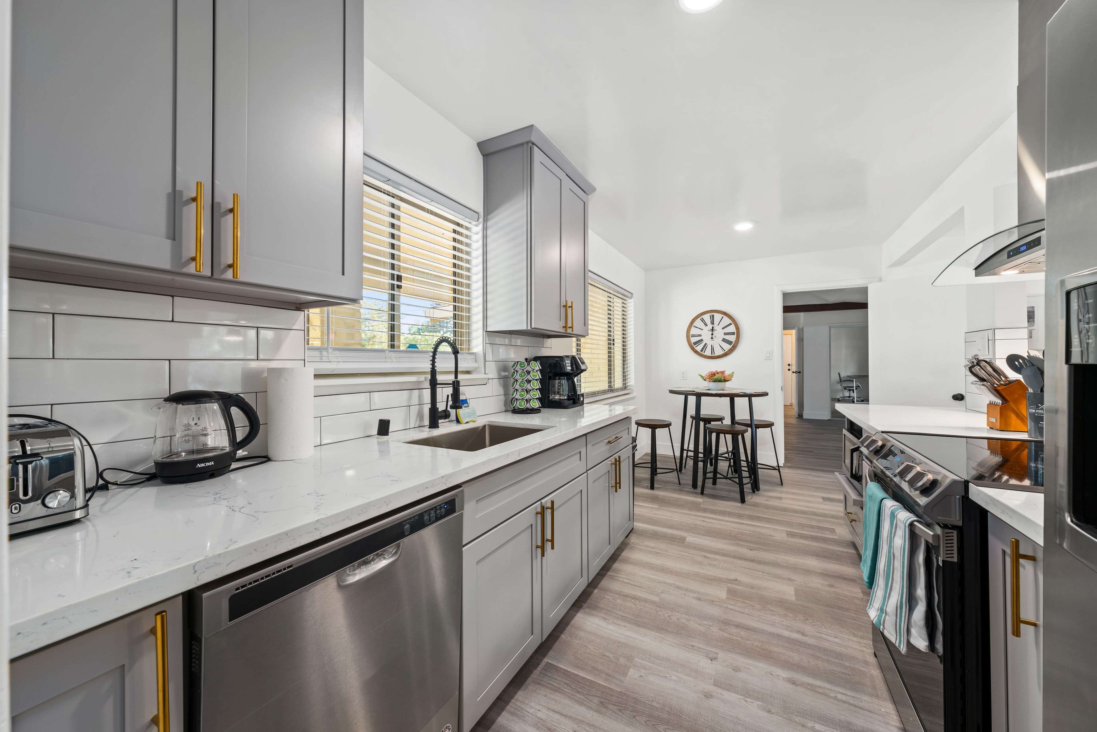 A modern kitchen featuring gray cabinets, a white countertop, stainless steel appliances, and a small dining area with a round table.