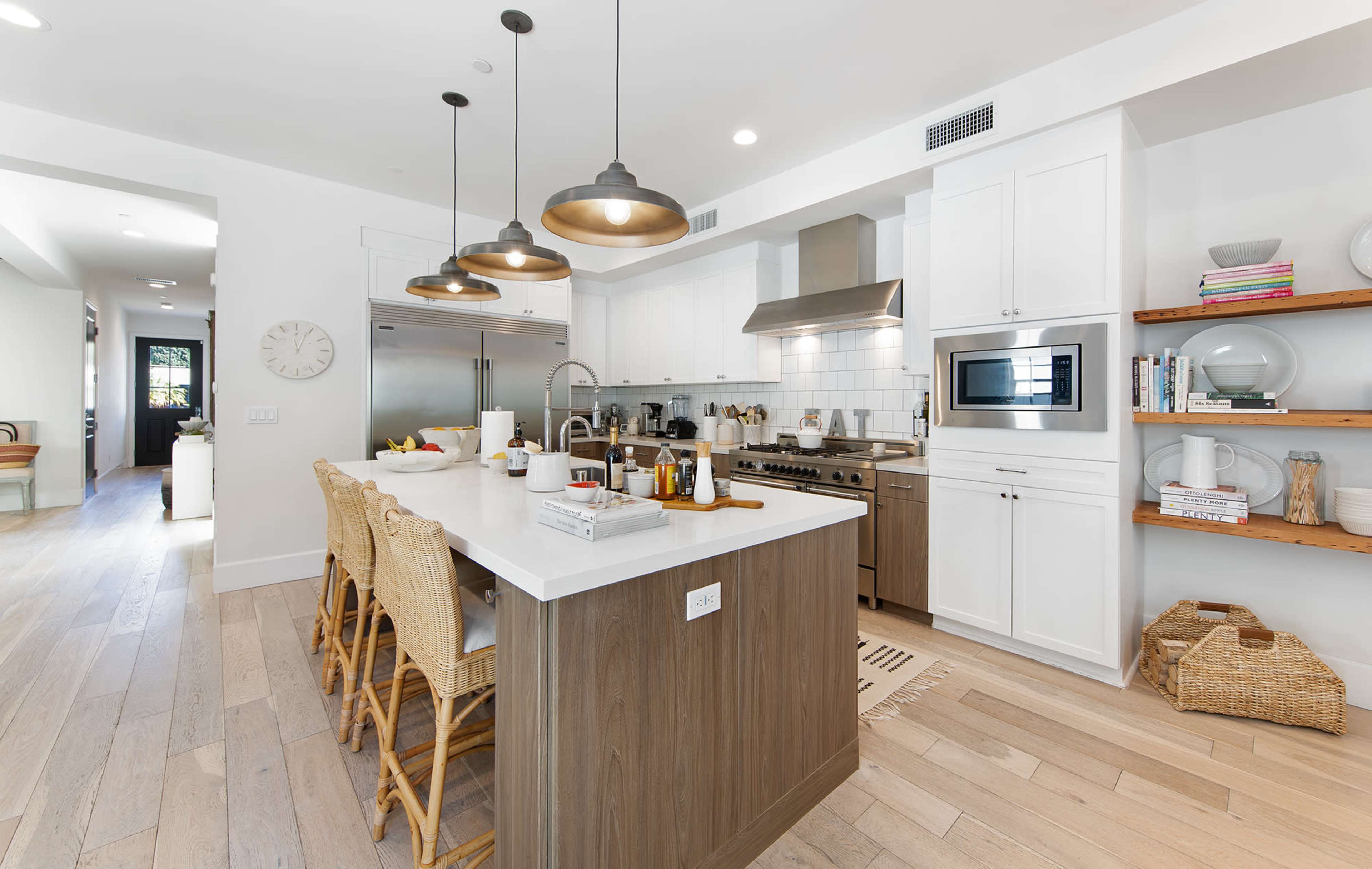 A modern kitchen features a central island with bar stools, stainless steel appliances, and wooden shelves displaying kitchen items.