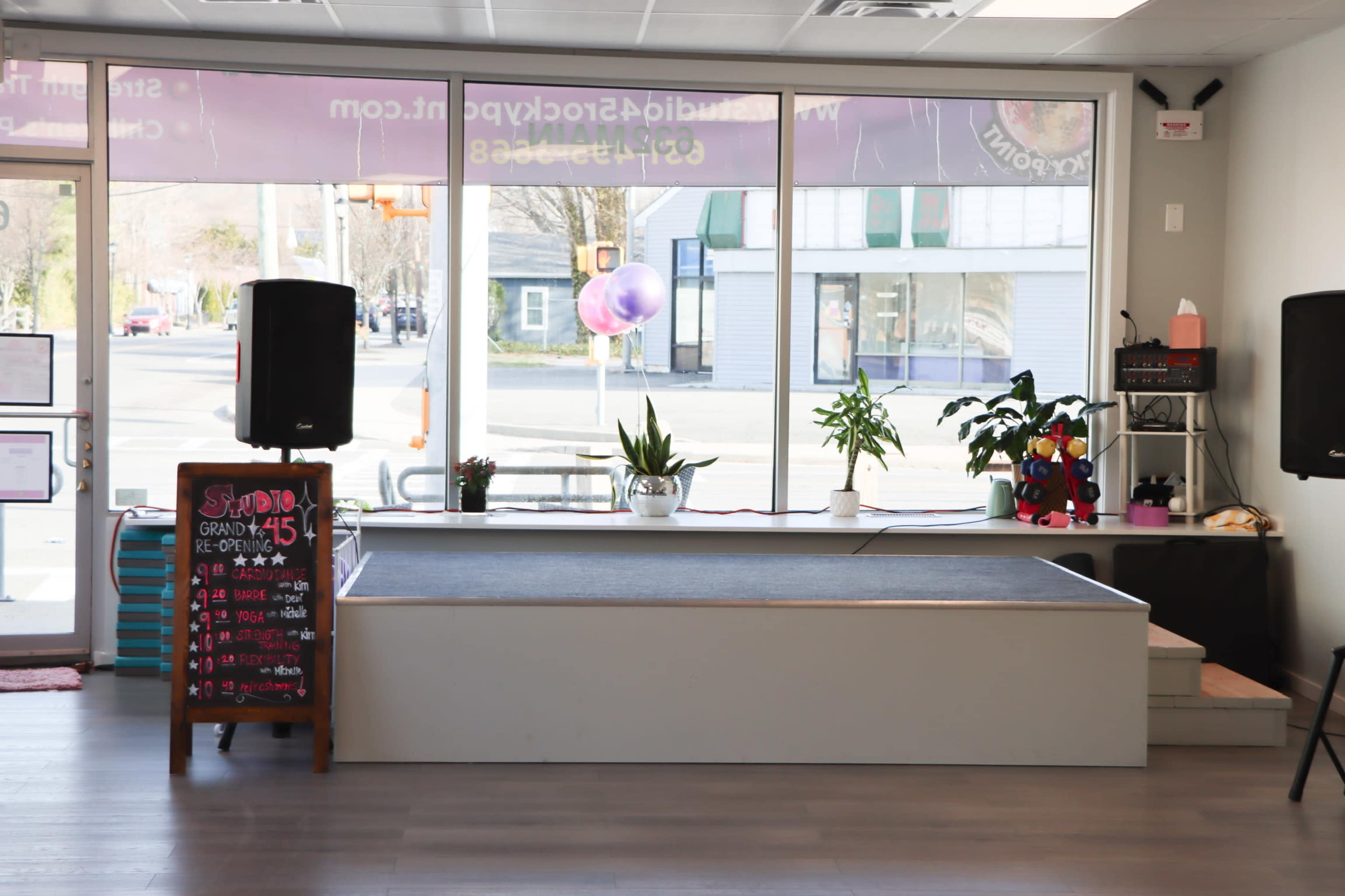 The image shows a visually clean, well-lit interior of a studio with a performance stage, plants, and equipment along the window.