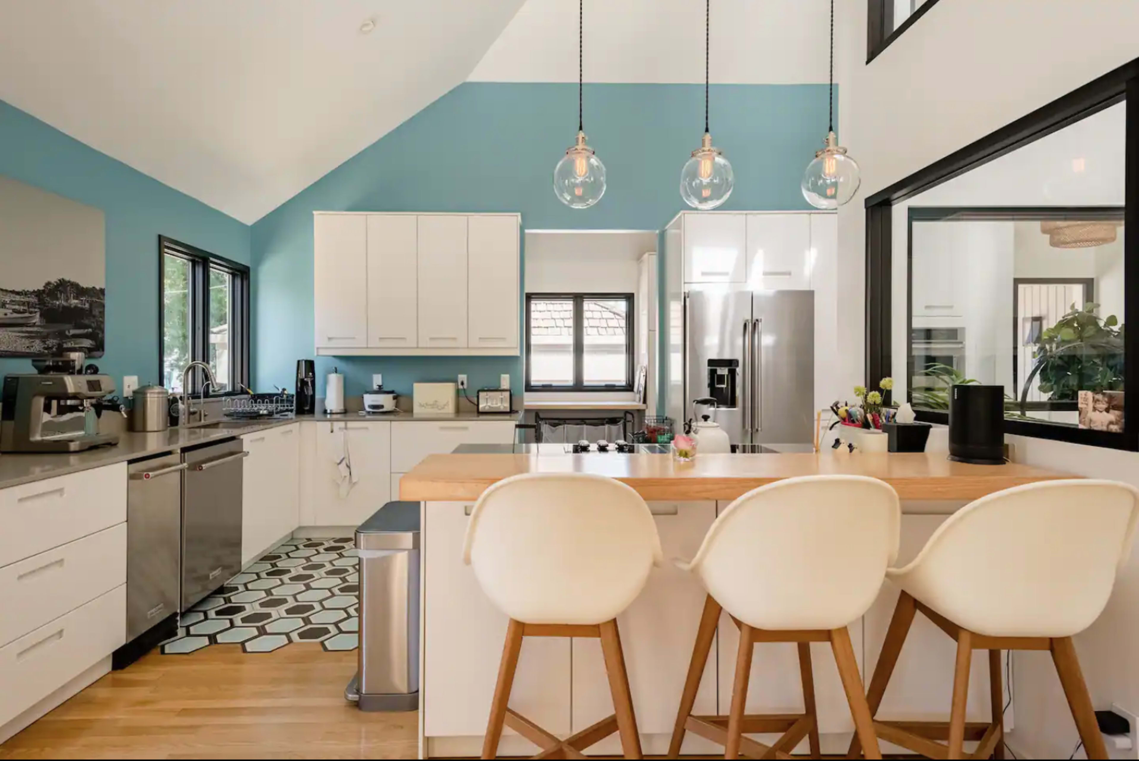A modern kitchen features a combination of light cabinetry, a blue accent wall, and a wooden island with three bar stools.