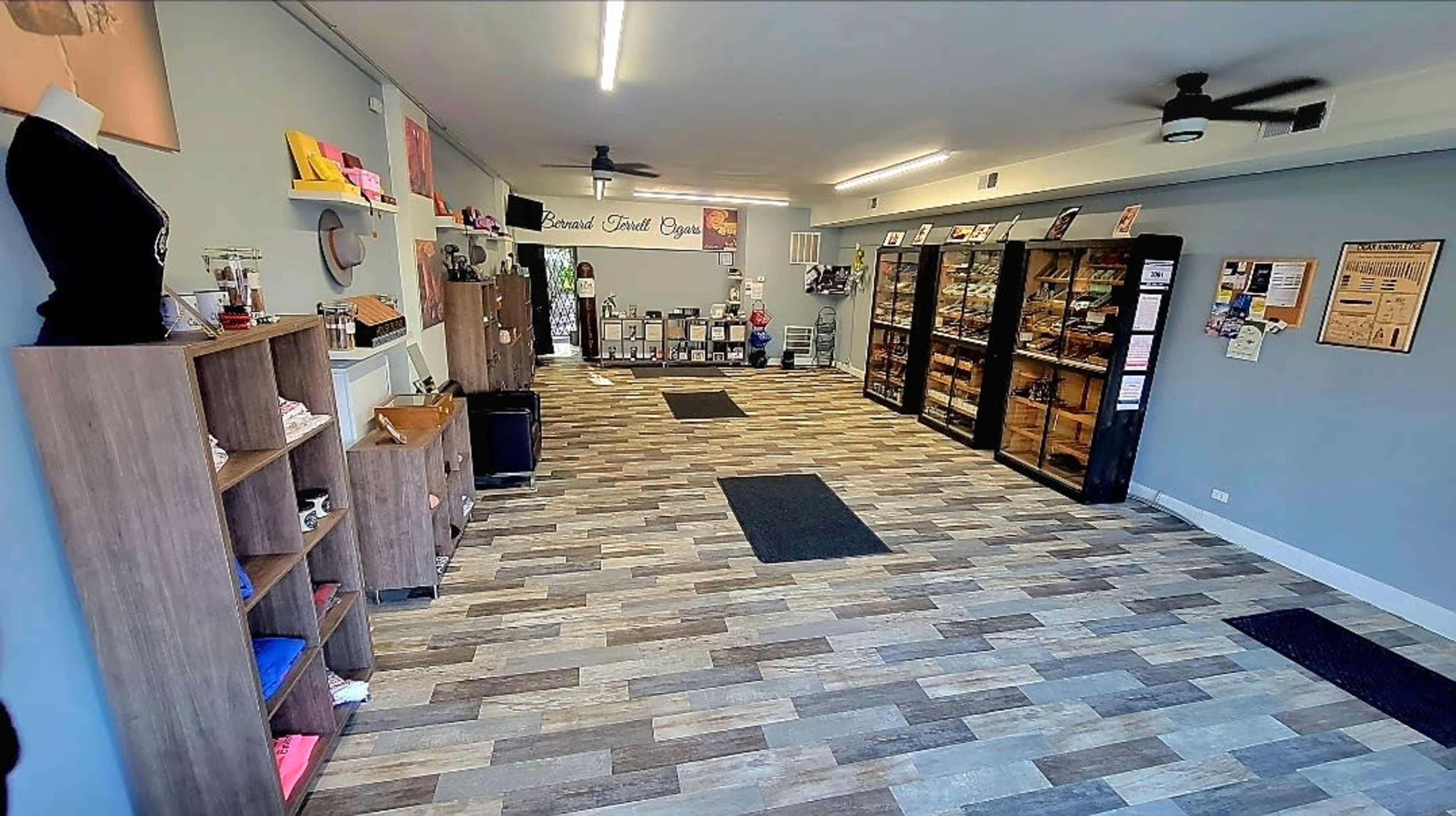 The image shows a retail space with a wooden floor, shelves displaying products on the right, and a reception area with clothing items on the left.