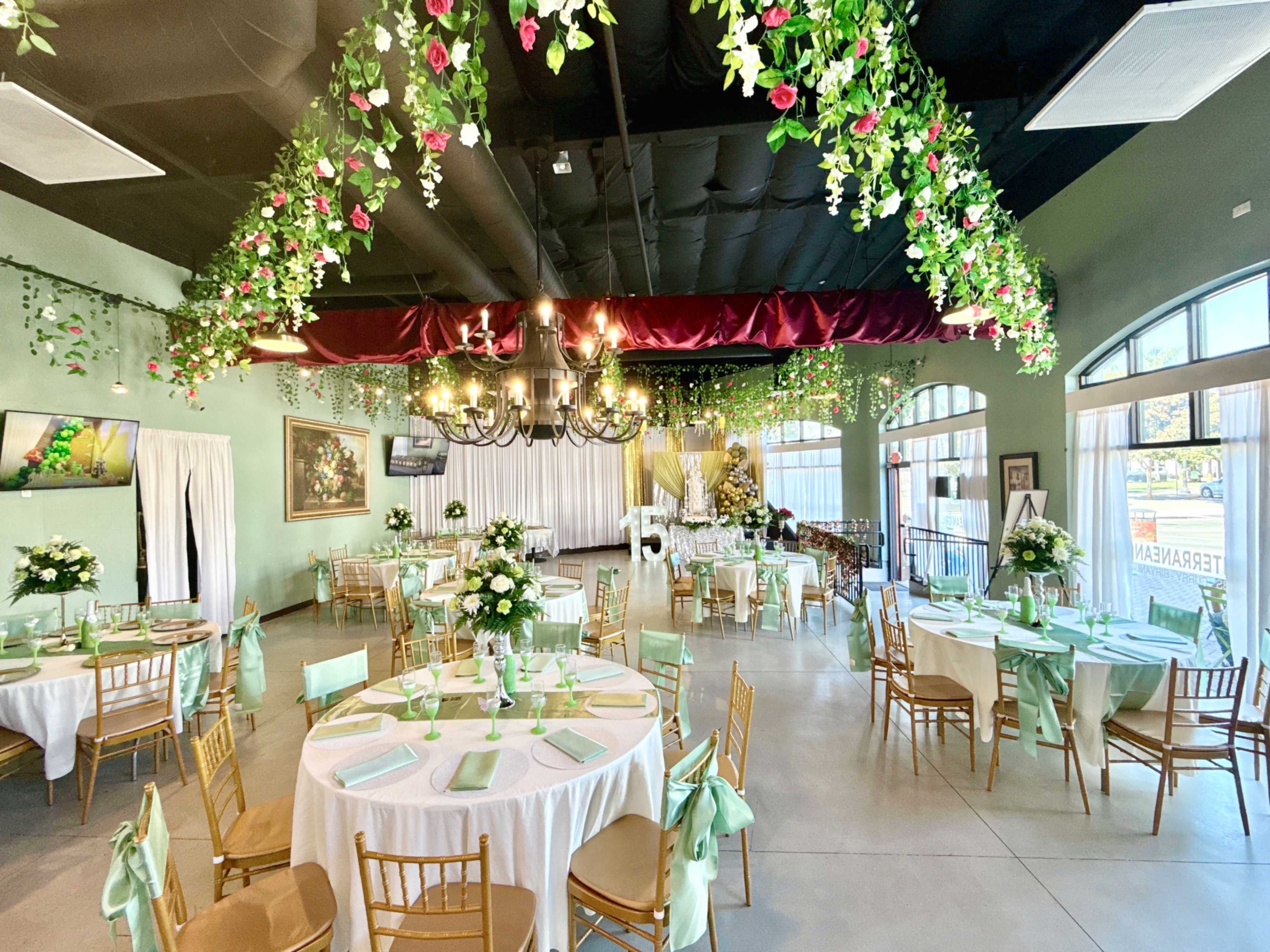 The image shows an elegantly decorated banquet hall with tables set for an event, featuring floral arrangements and green accents.