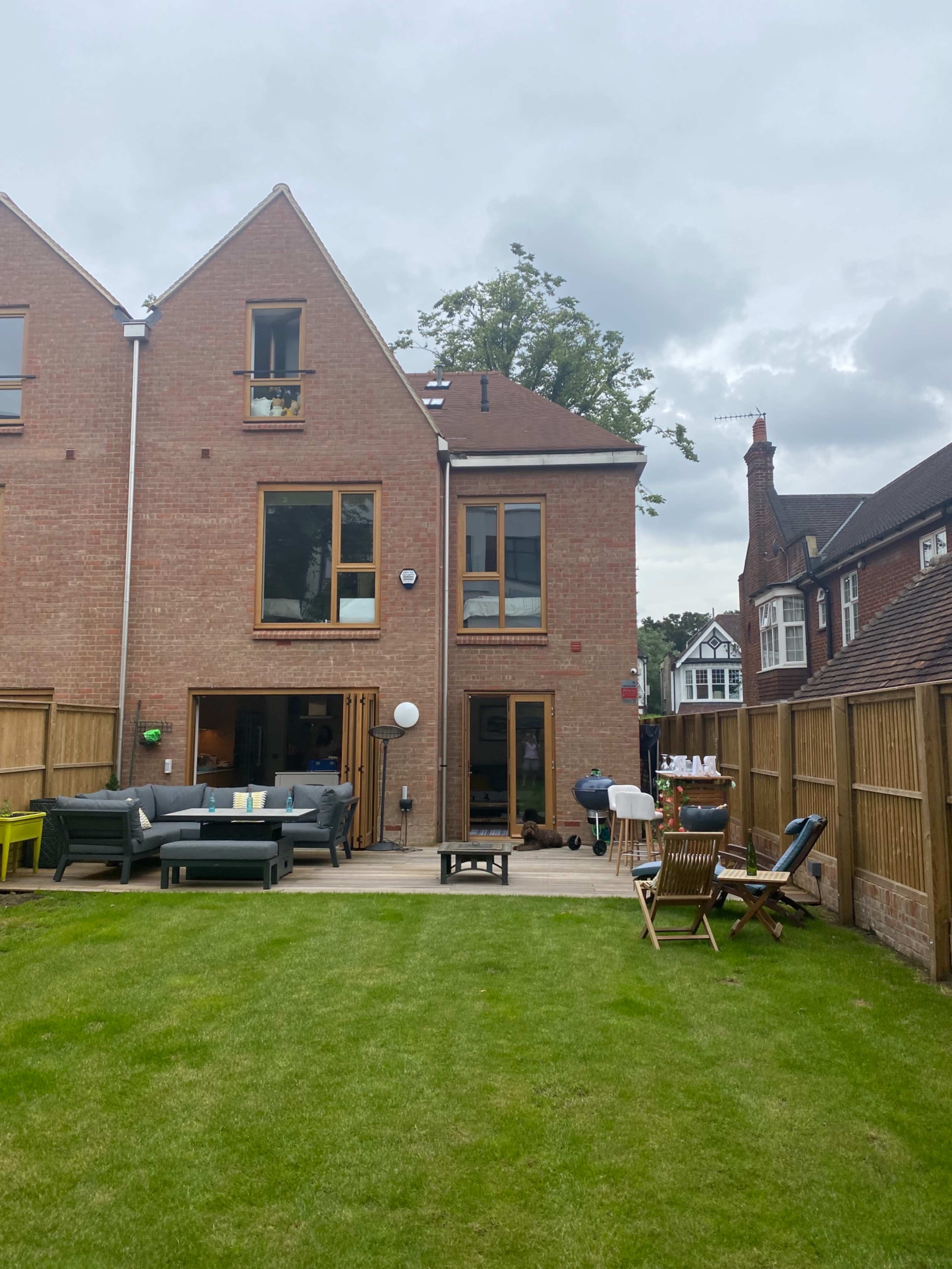 A well-kept backyard features a lawn, patio area, and two residential buildings with large windows.