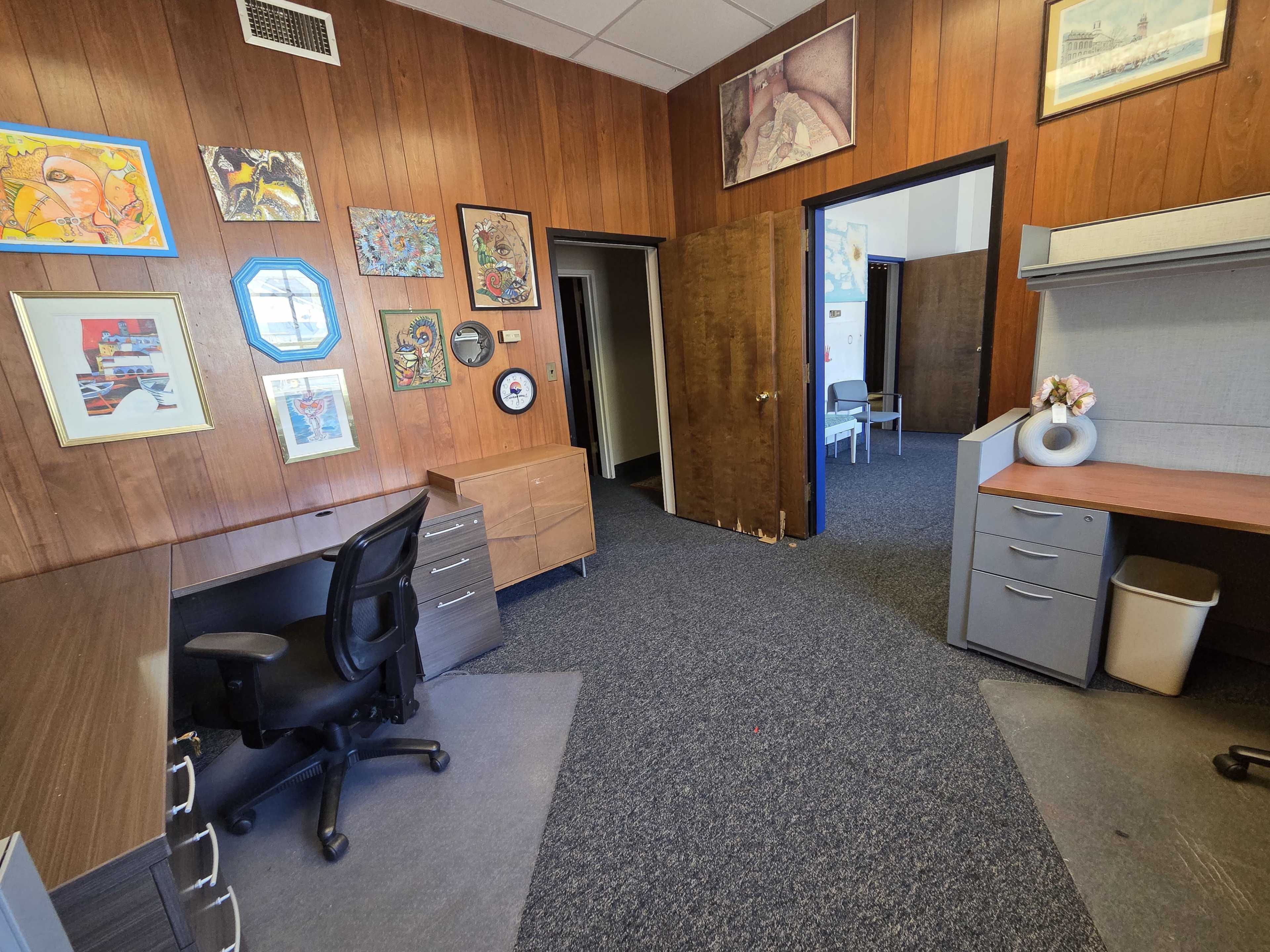 The image shows an office space with wooden paneling, two desks, and various framed artworks on the walls.