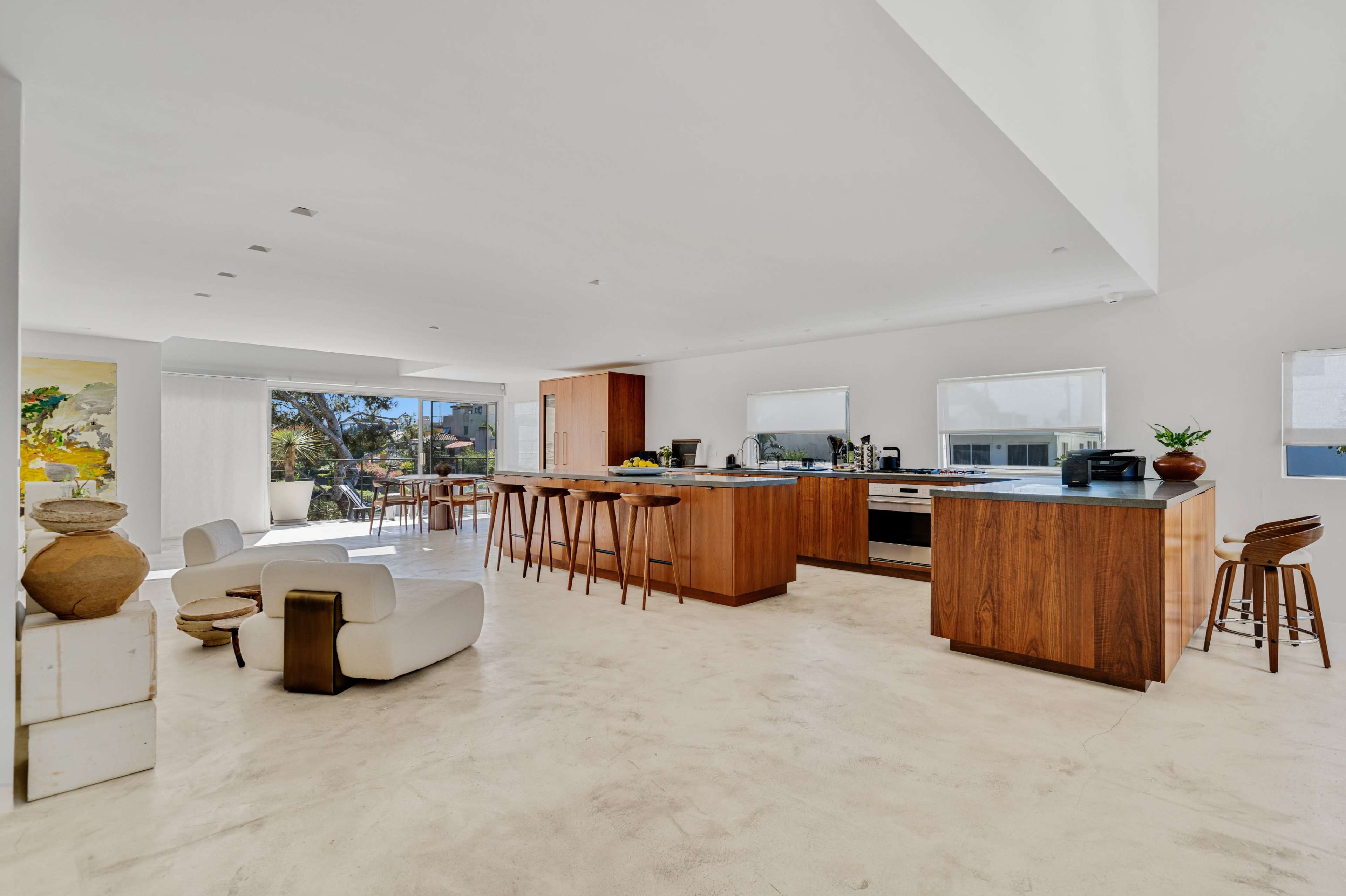 A spacious, modern kitchen features a large island with wooden cabinetry, bar stools, and large windows allowing natural light to illuminate the room.