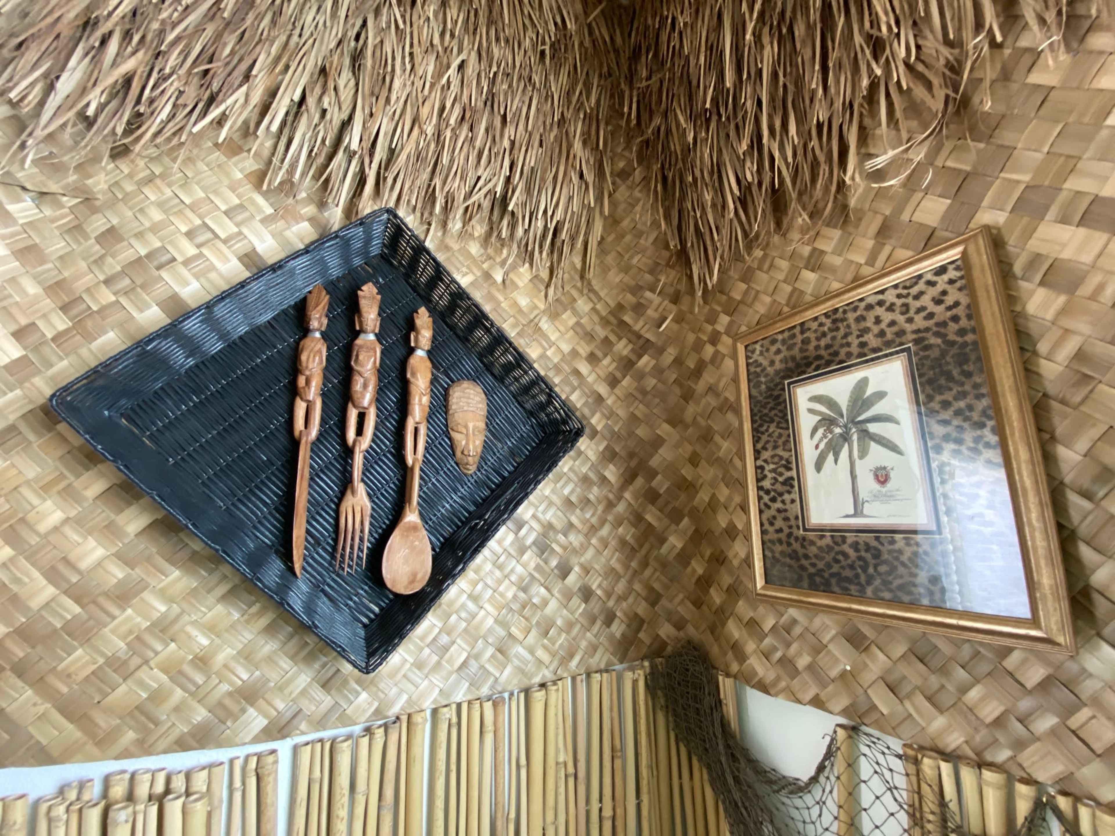 A corner of a textured wall adorned with a woven grass-like surface, featuring wooden utensils and a framed botanical print.