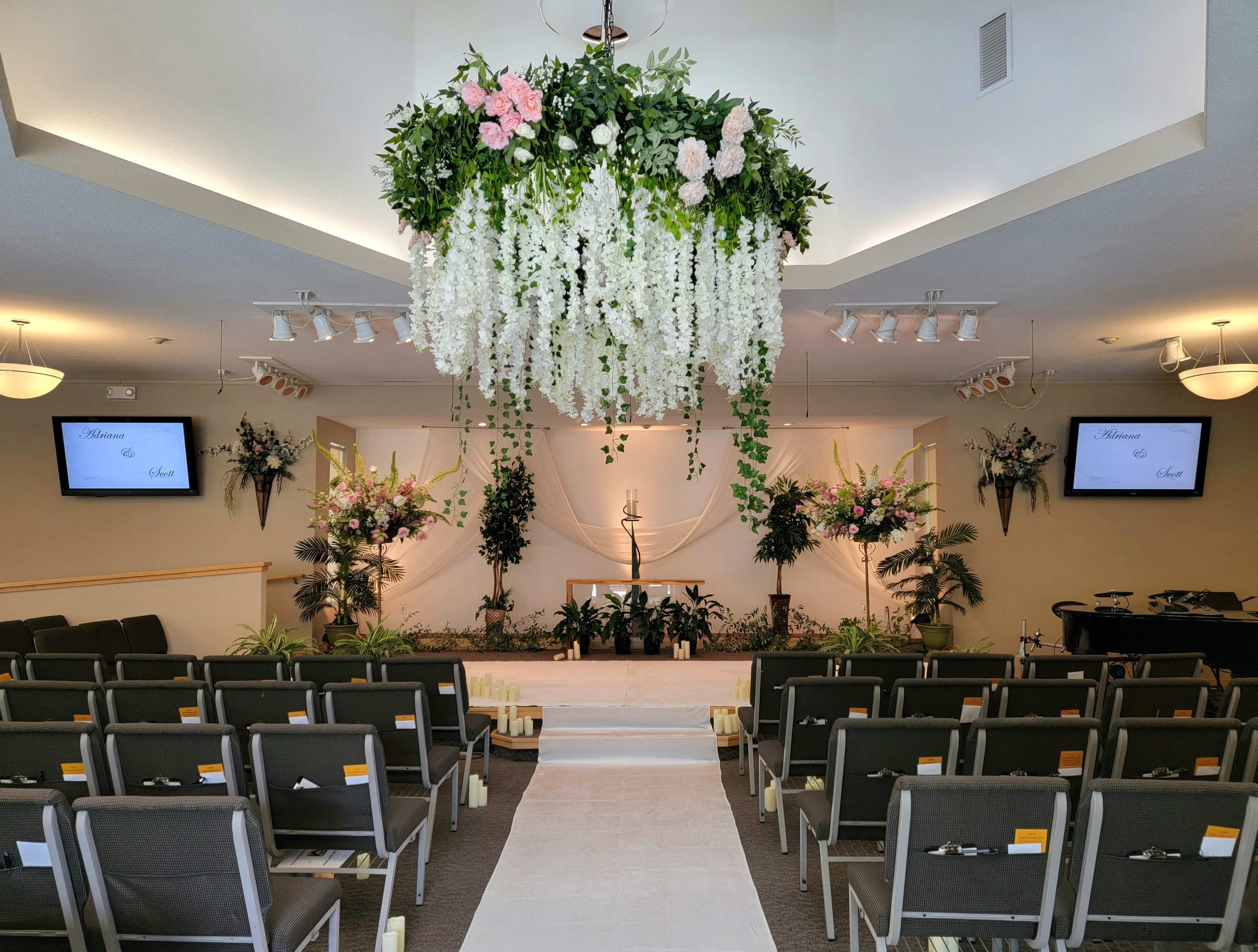 A decorated indoor ceremony space featuring floral arrangements, a central altar with a candle, and seating arranged in rows facing the front.