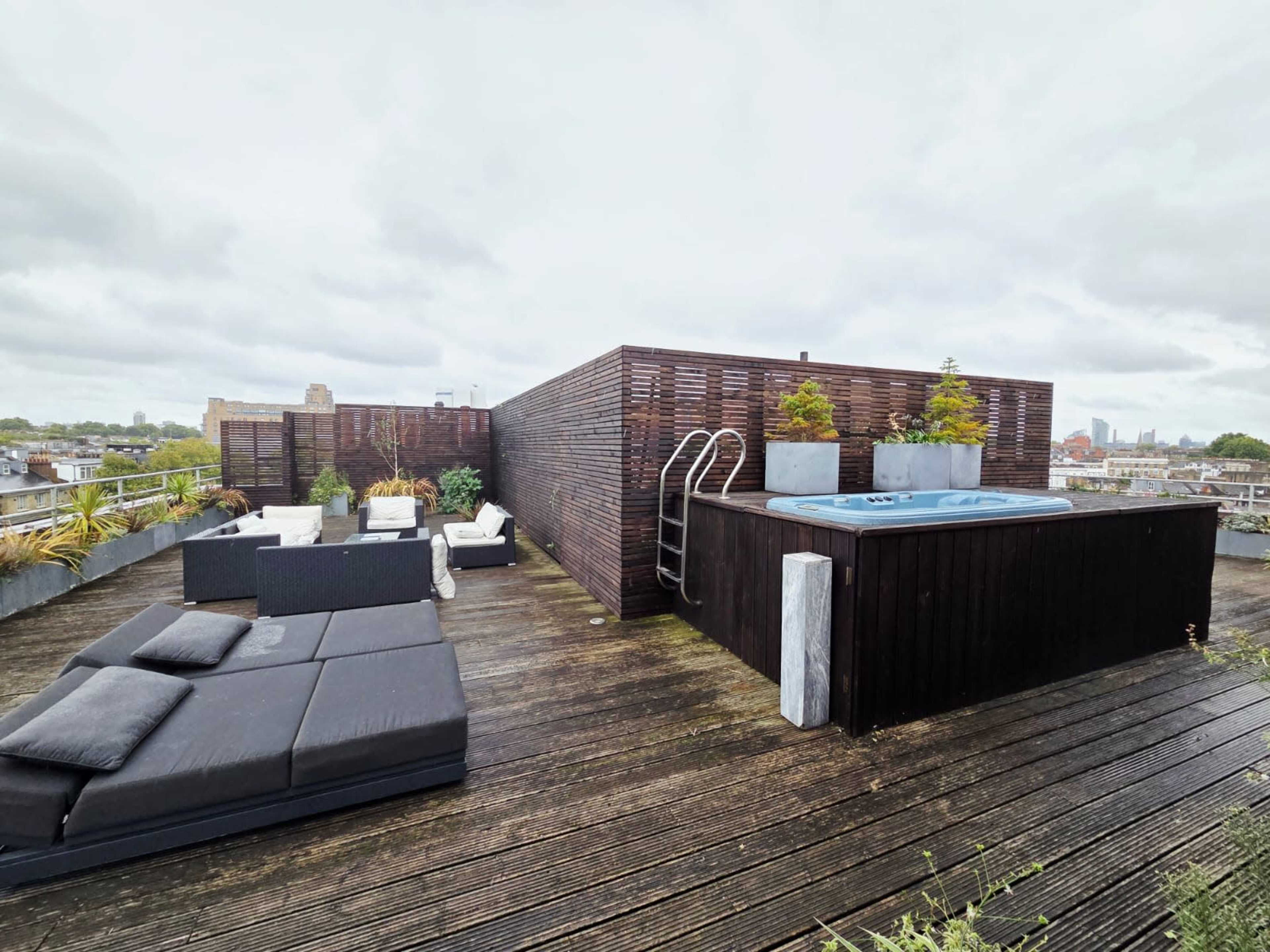 The rooftop terrace features a wooden deck with lounge seating, planters, and a hot tub.