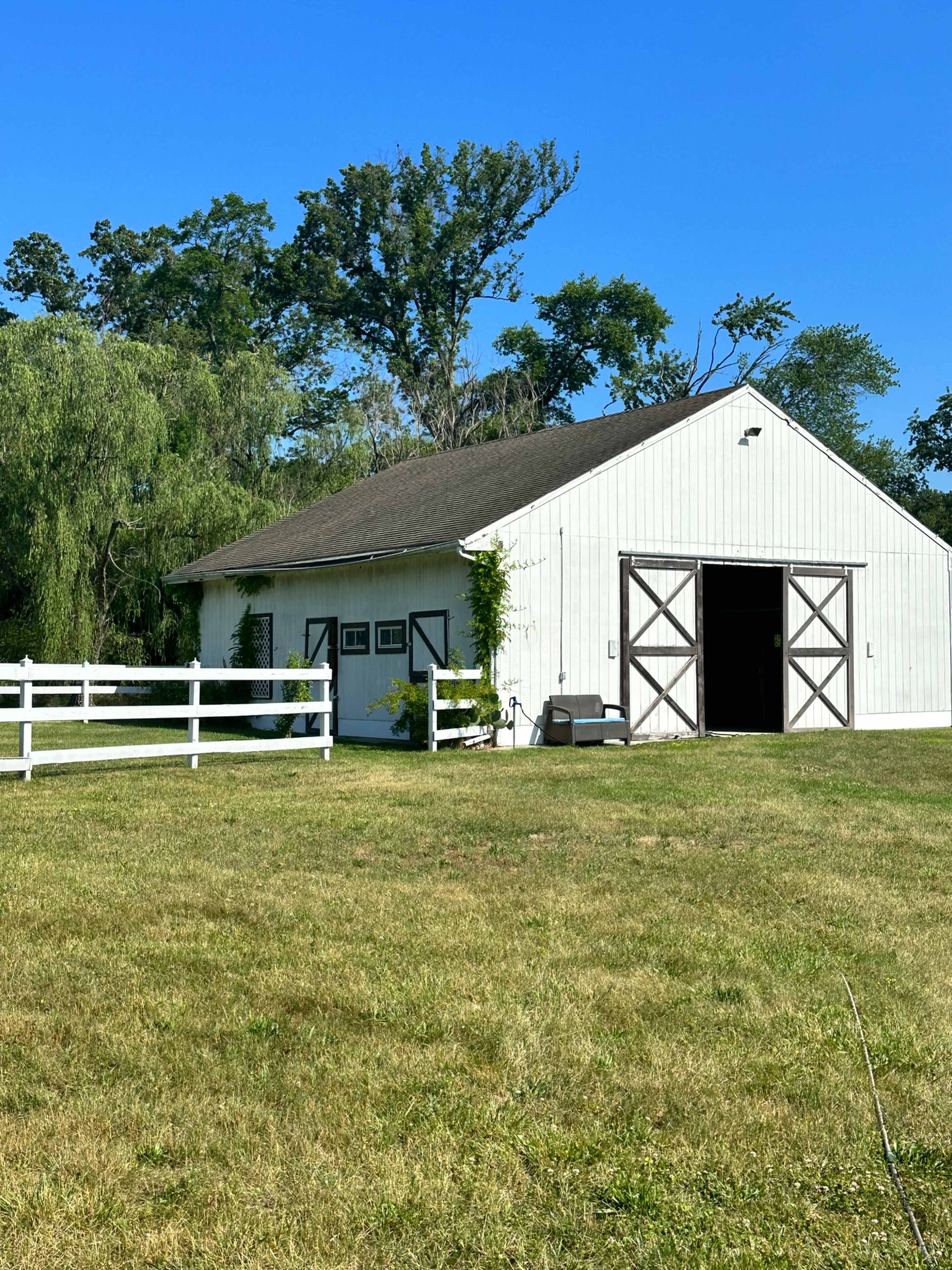 A white barn with a green lawn and a white fence in front, set against a clear blue sky.
