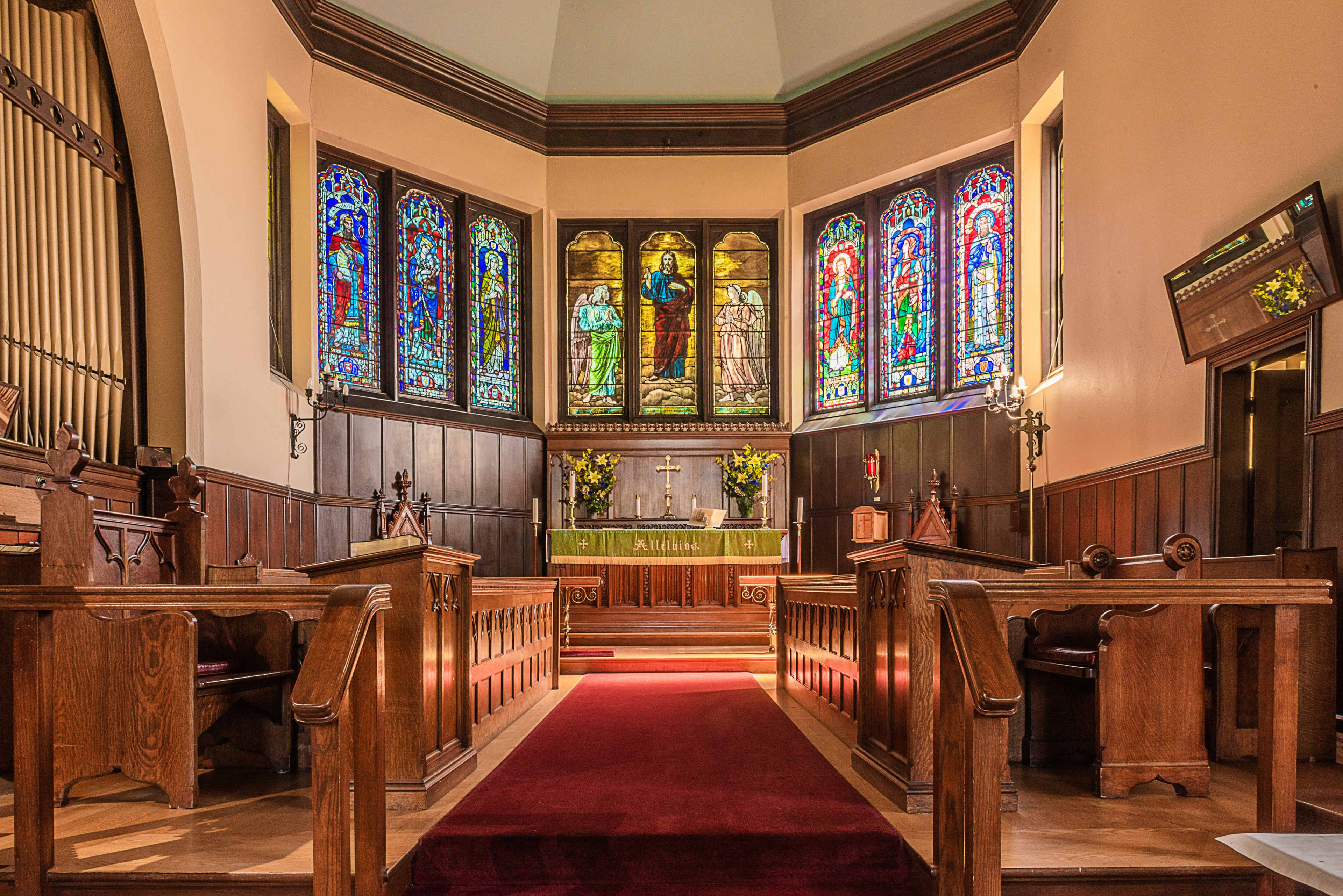 The interior of a church features wooden pews, colorful stained glass windows, and an altar adorned with flowers.